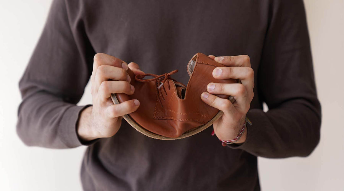 Man holding and flexing a pair of brown genuine leather barefoot shoes, showcasing their flexibility and lightweight design. Discover the benefits of barefoot shoes a pelanir.com.