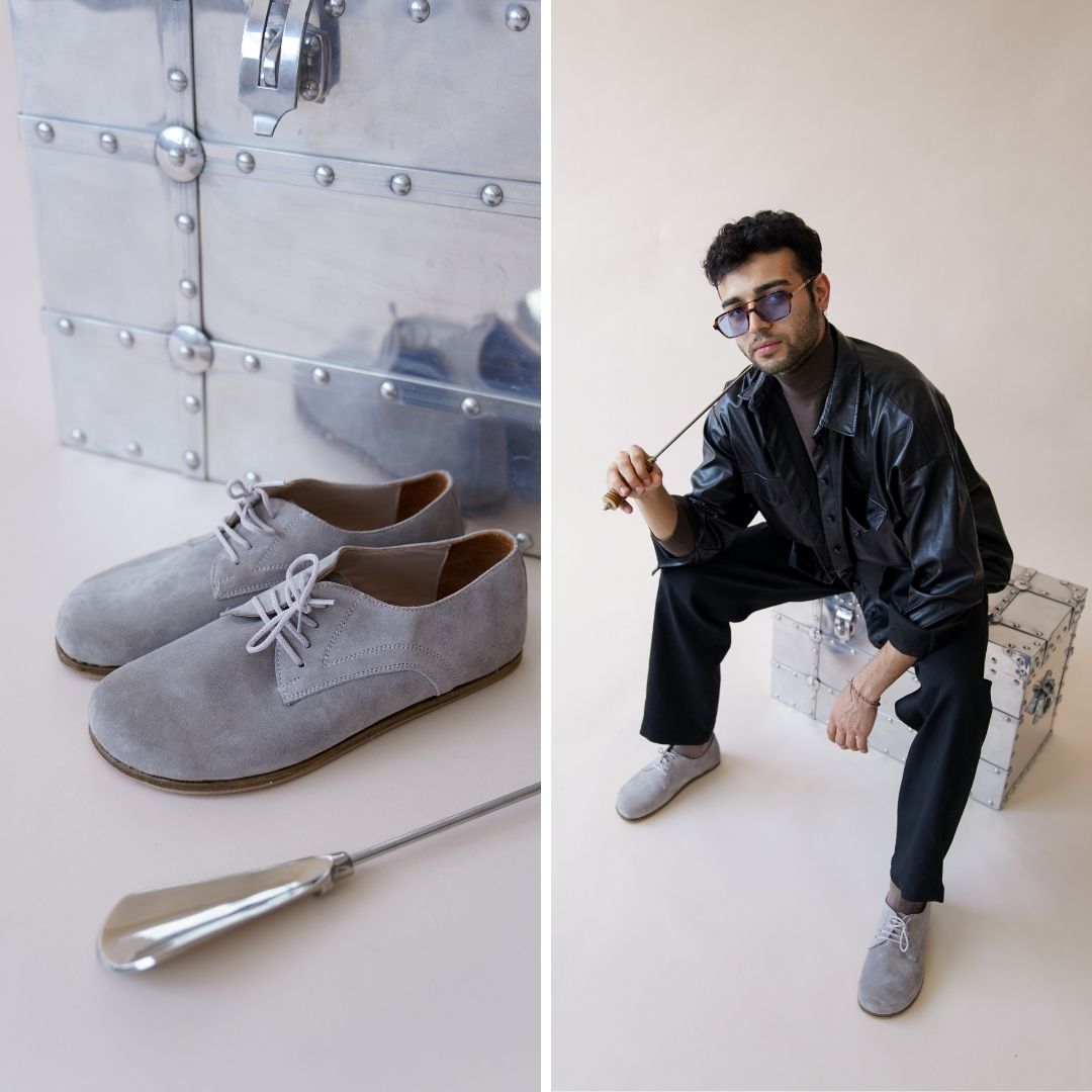 Model sitting with Locris Leather Barefoot Men's Oxfords in gray suede, paired with black pants, showcasing their stylish versatility.