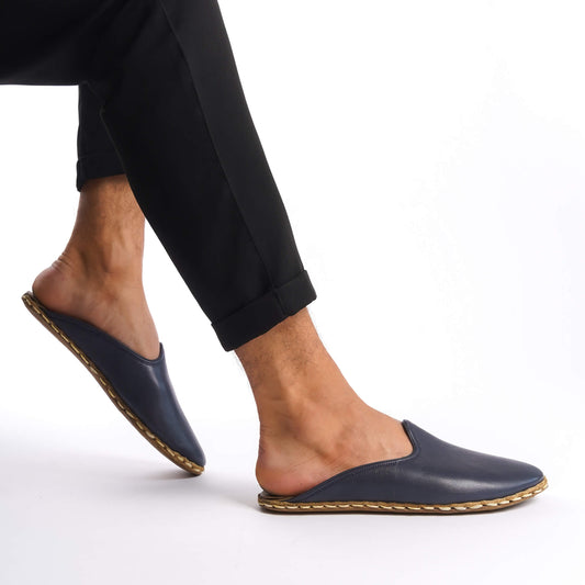 Person lifting foot while wearing navy blue leather slippers.