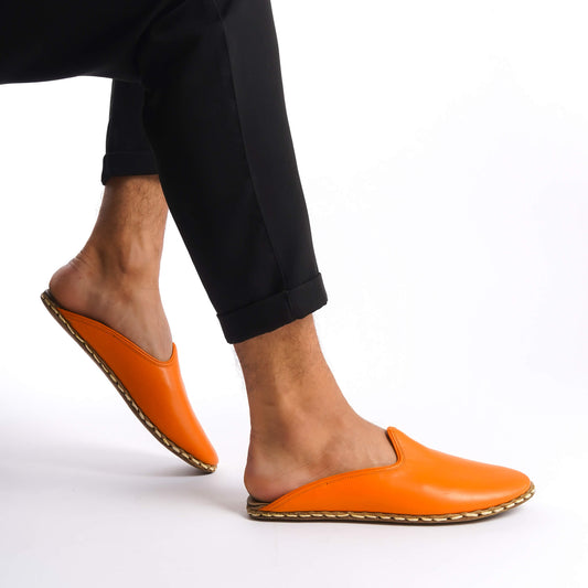 Person lifting foot while wearing bright orange leather slippers.