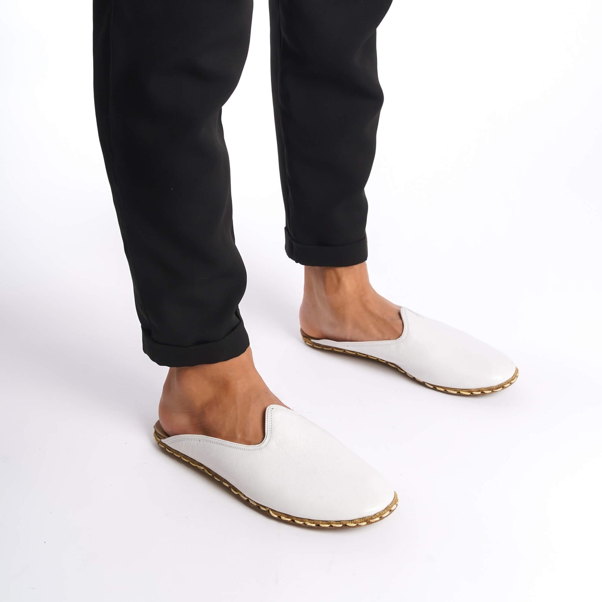 Person standing in white leather slippers with natural leather soles, zero drop design, and edge stitching.