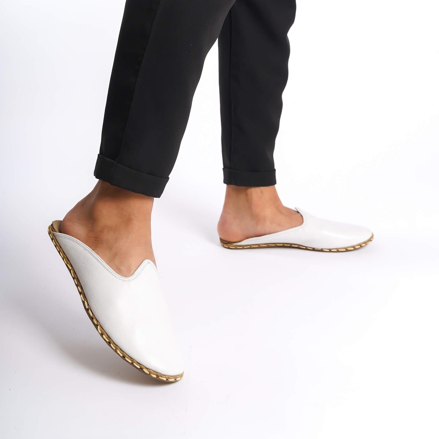 Person walking in white leather slippers with natural leather soles, zero drop design, and edge stitching.