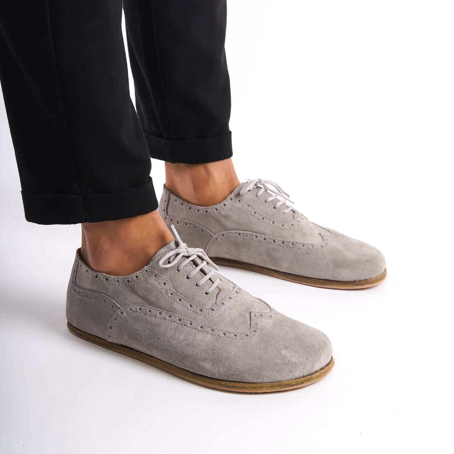 Man posing in gray suede barefoot Oxfords, emphasizing their classic brogue design and fit.