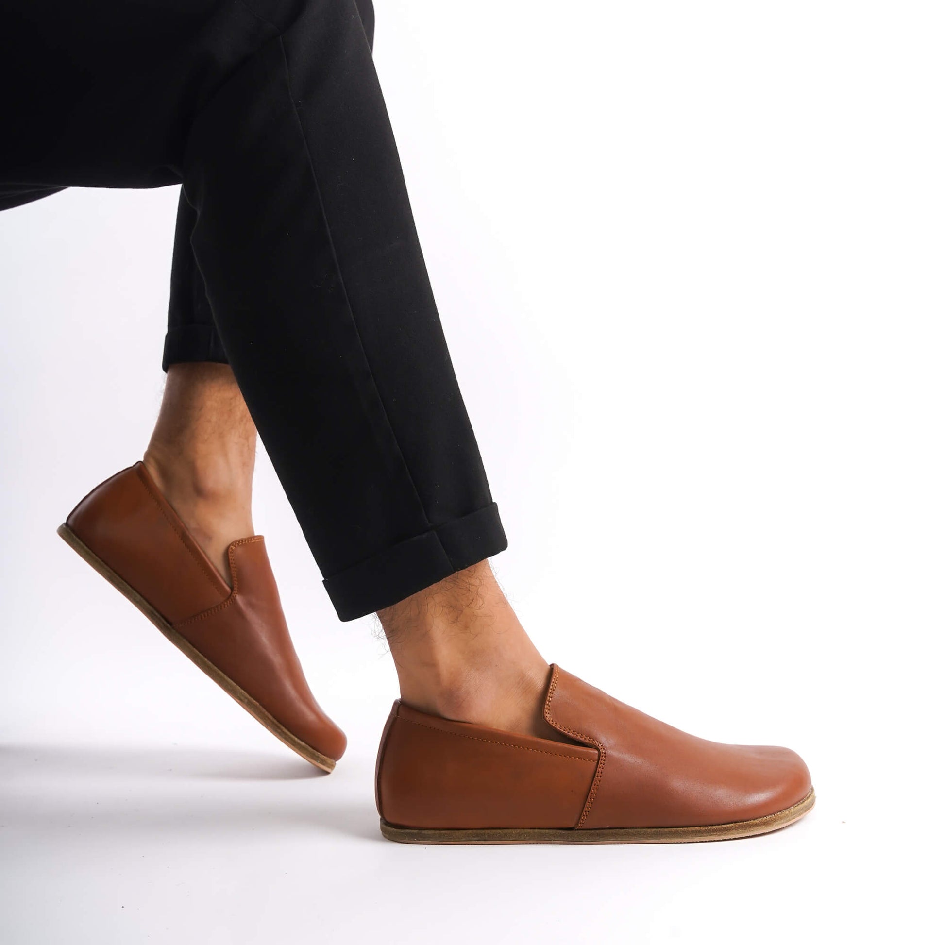 Tan brown Aeolia Leather Barefoot Men's Loafers shown on feet with black pants, emphasizing the sleek and versatile design.