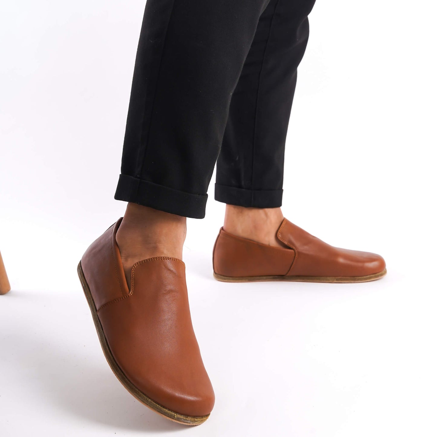 Tan brown Aeolia Leather Barefoot Men's Loafers with a minimalist design and wide toe box, shown on feet with black pants.