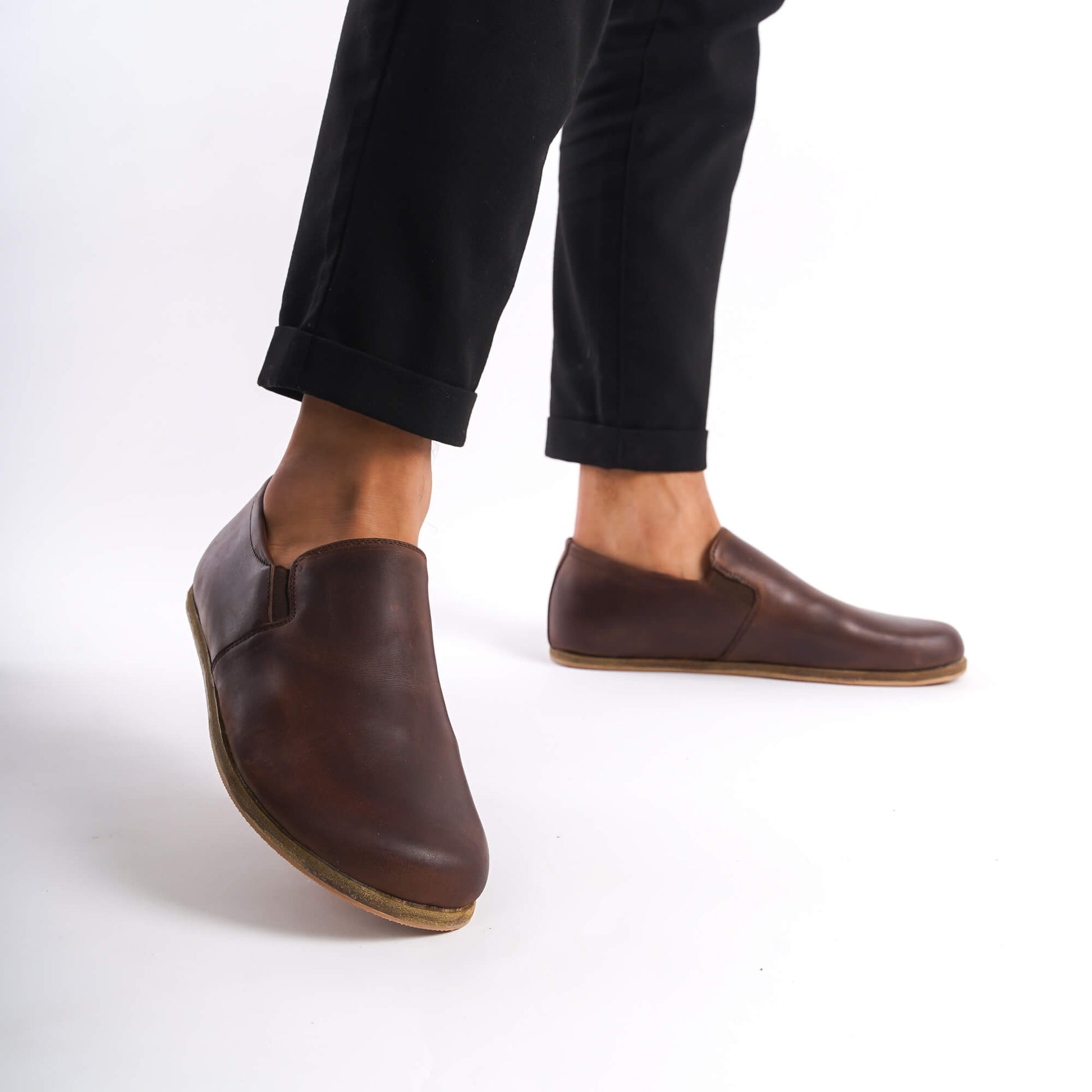 Close-up of a person wearing brown Ionia Leather Barefoot Men Loafers with black pants, highlighting the comfortable fit and natural design.