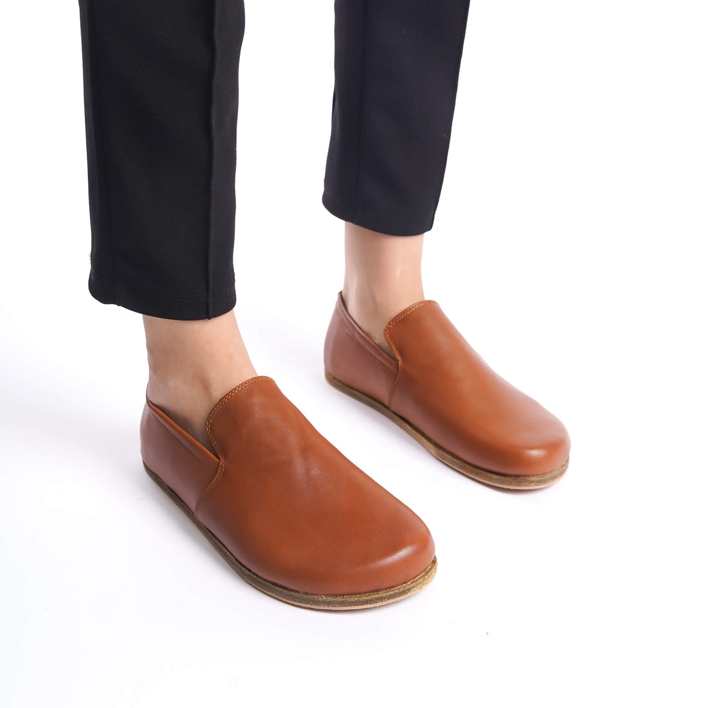 Close-up of Aeolia tan brown leather barefoot women loafers, paired with black pants.