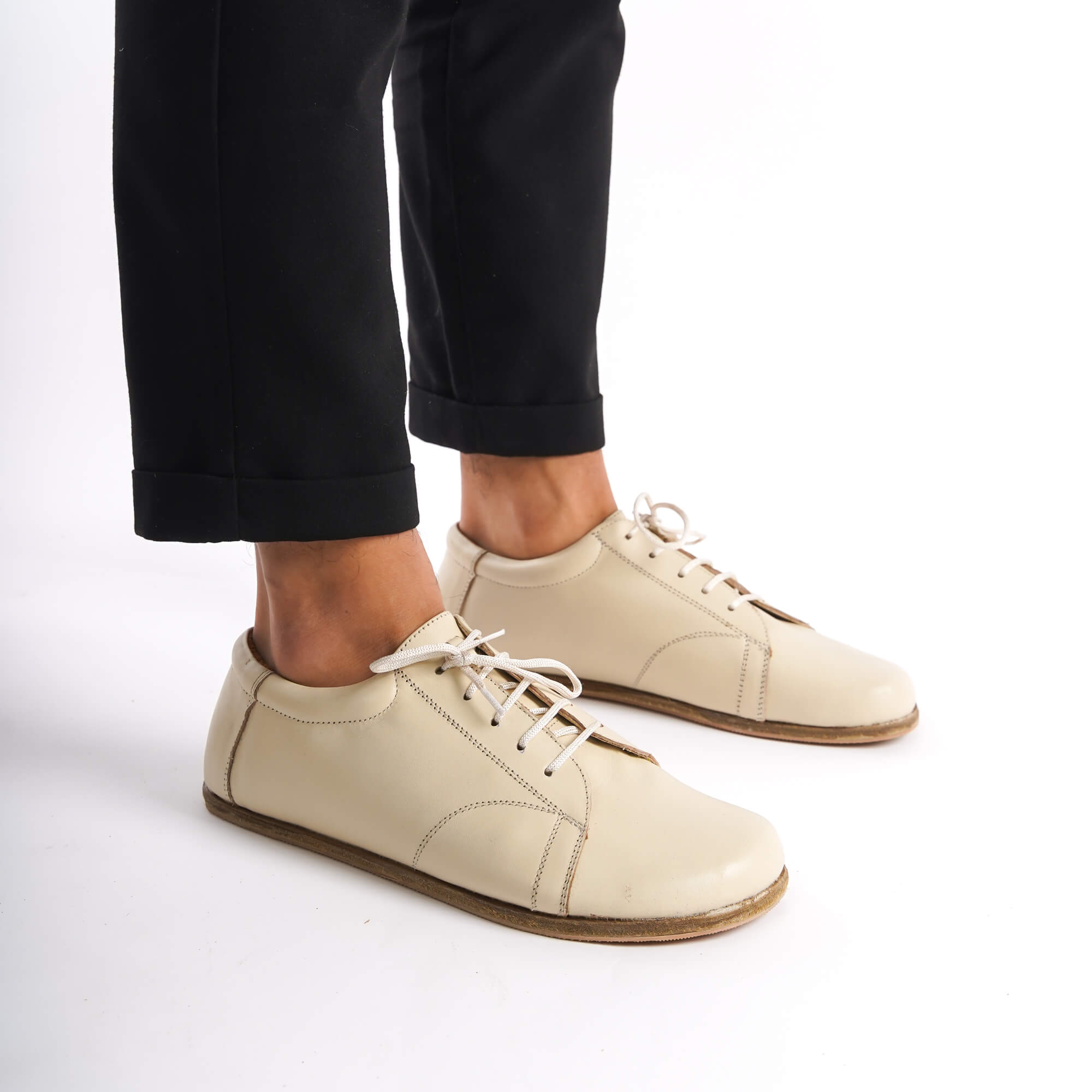 Lydia Leather Barefoot Men's Sneakers in Beige with Black Pants, showcasing their sleek design and comfort.
