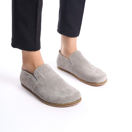 Side view of gray suede barefoot loafers paired with black pants, showcasing their sleek design.