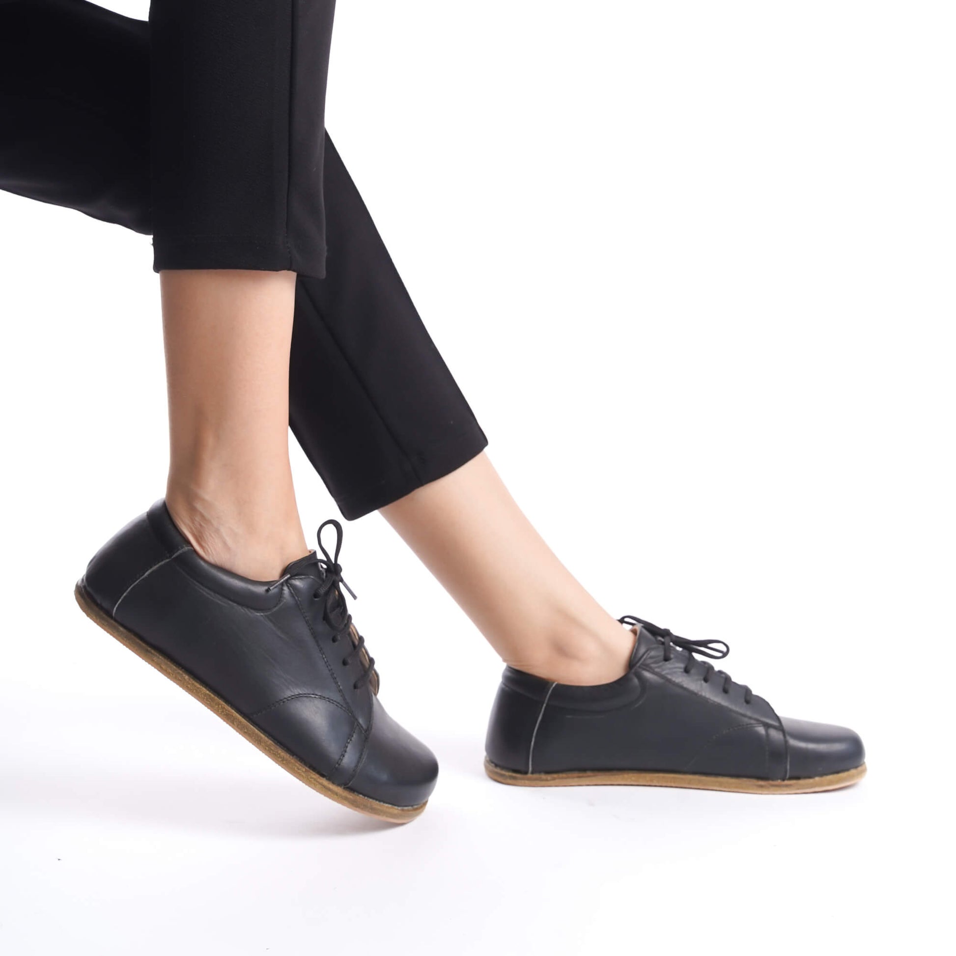 Model wearing black Lydia Leather Barefoot Women's Sneakers, demonstrating flexibility and minimalist design.