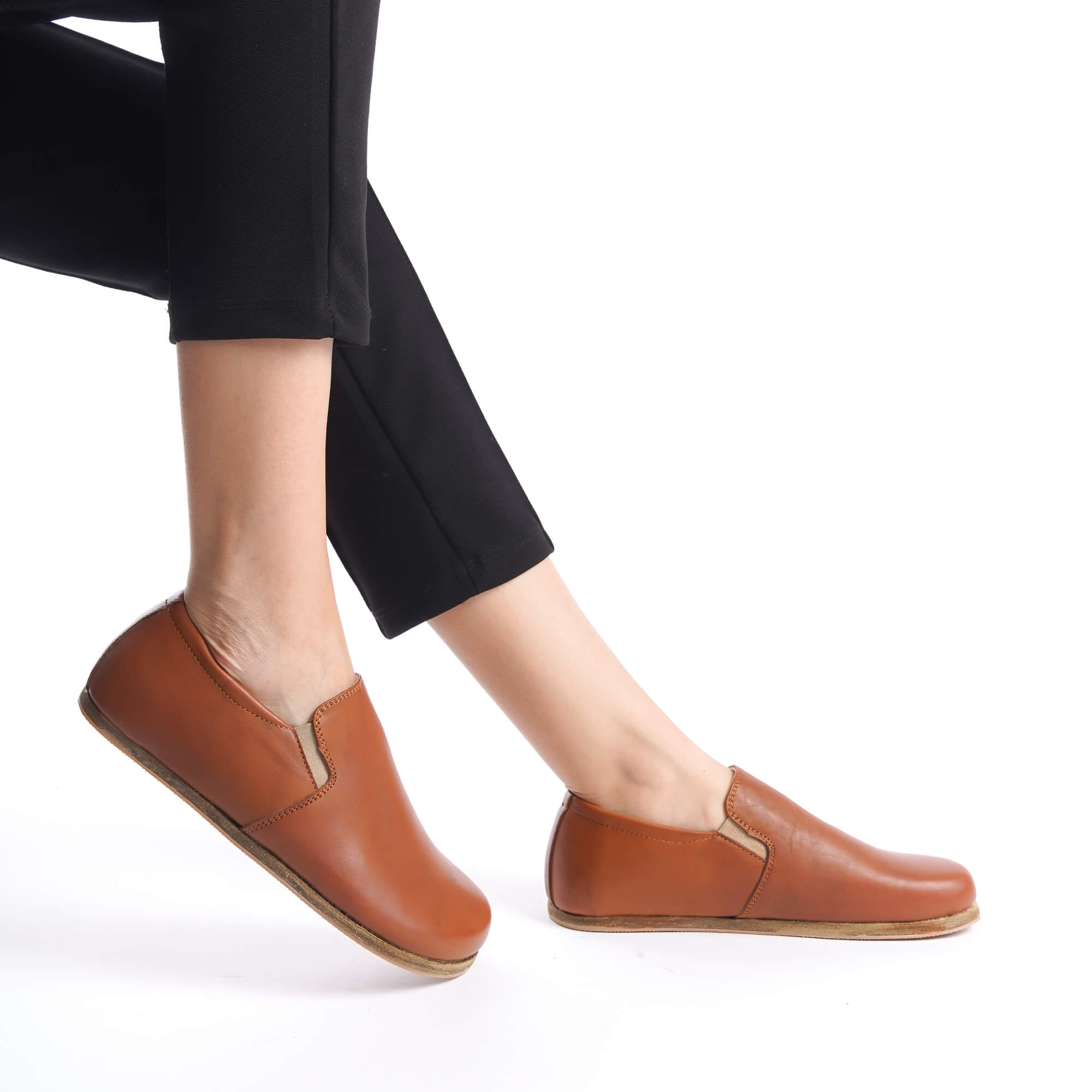 Tan brown Ionia leather barefoot women loafers, highlighted on a model with black pants, showing their stylish and comfortable fit.