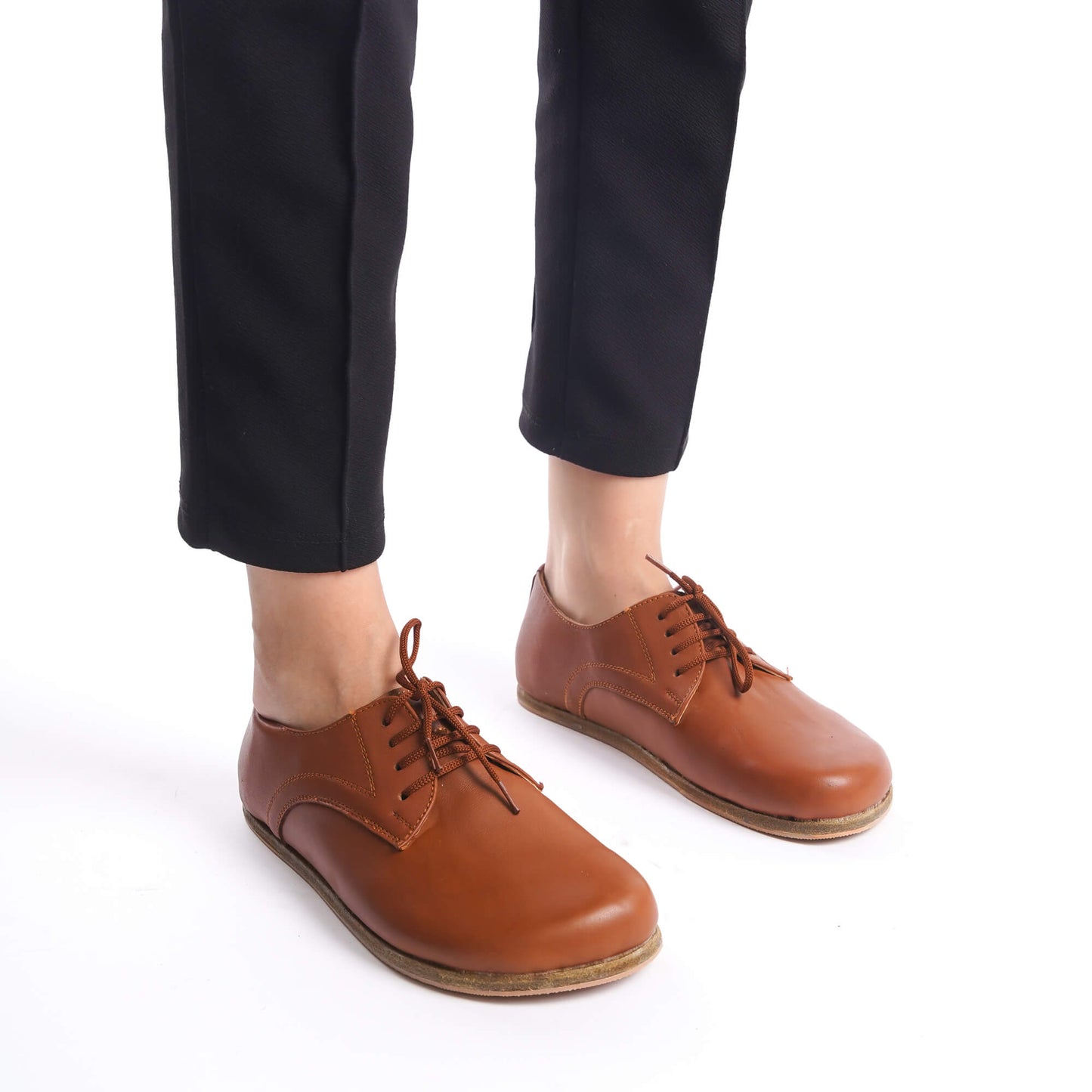 Model standing in tan brown leather barefoot women Oxfords, highlighting the shoes' sleek design and natural fit for everyday comfort.