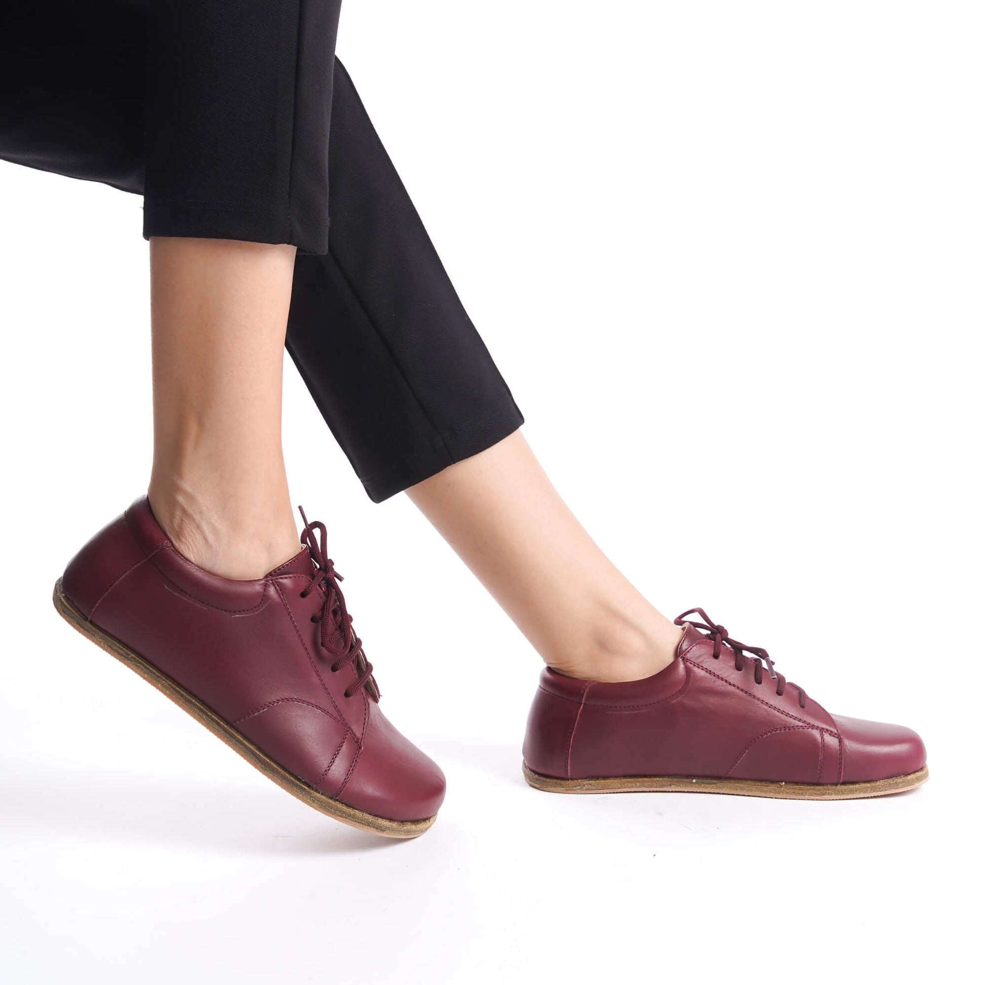 Close-up of burgundy barefoot women's sneakers in action, highlighting flexible sole and genuine leather construction.