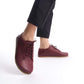 Woman wearing burgundy Lydia leather barefoot sneakers, paired with black pants, highlighting the sleek and modern look.