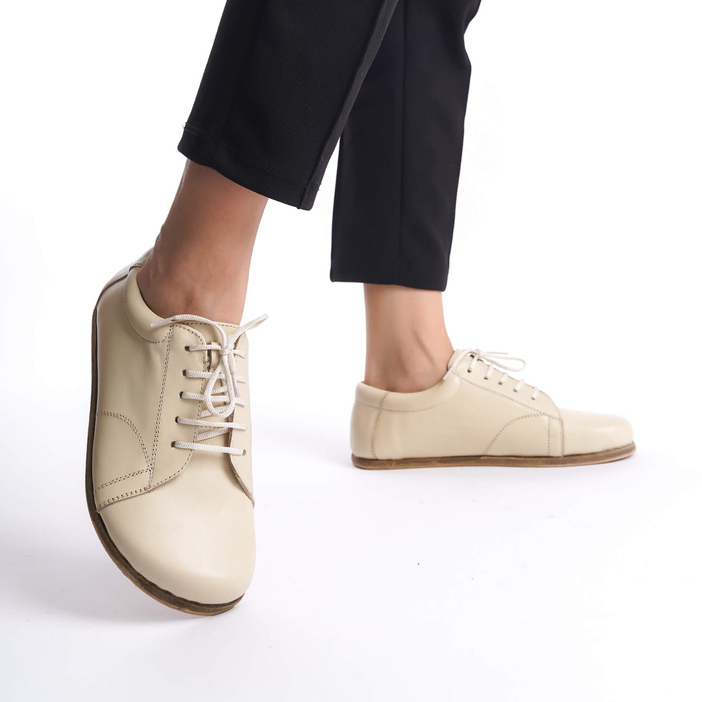 Close-up of model standing in beige leather barefoot women's sneakers, perfect for showcasing flexibility and foot health benefits.