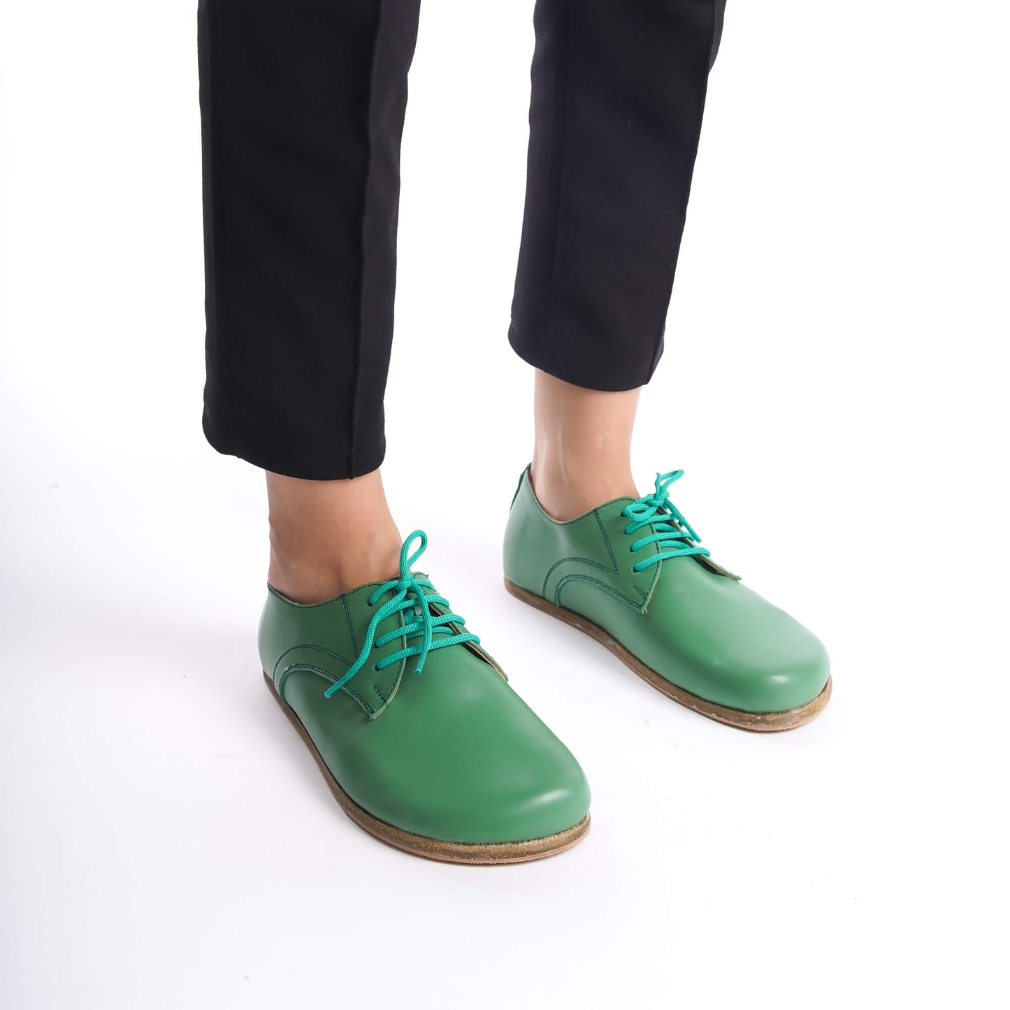 A close-up shot of green leather barefoot Oxfords worn with black pants, showcasing the shoes' natural fit and turquoise laces.