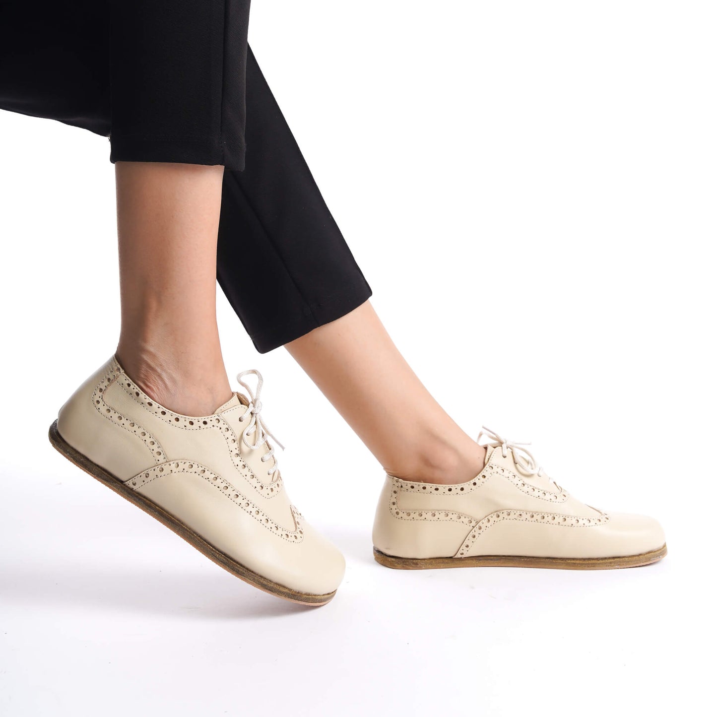 Side view of Doris Leather Barefoot Women's Oxfords in beige, worn by a model in black pants, highlighting the zero-drop design and flexibility.
