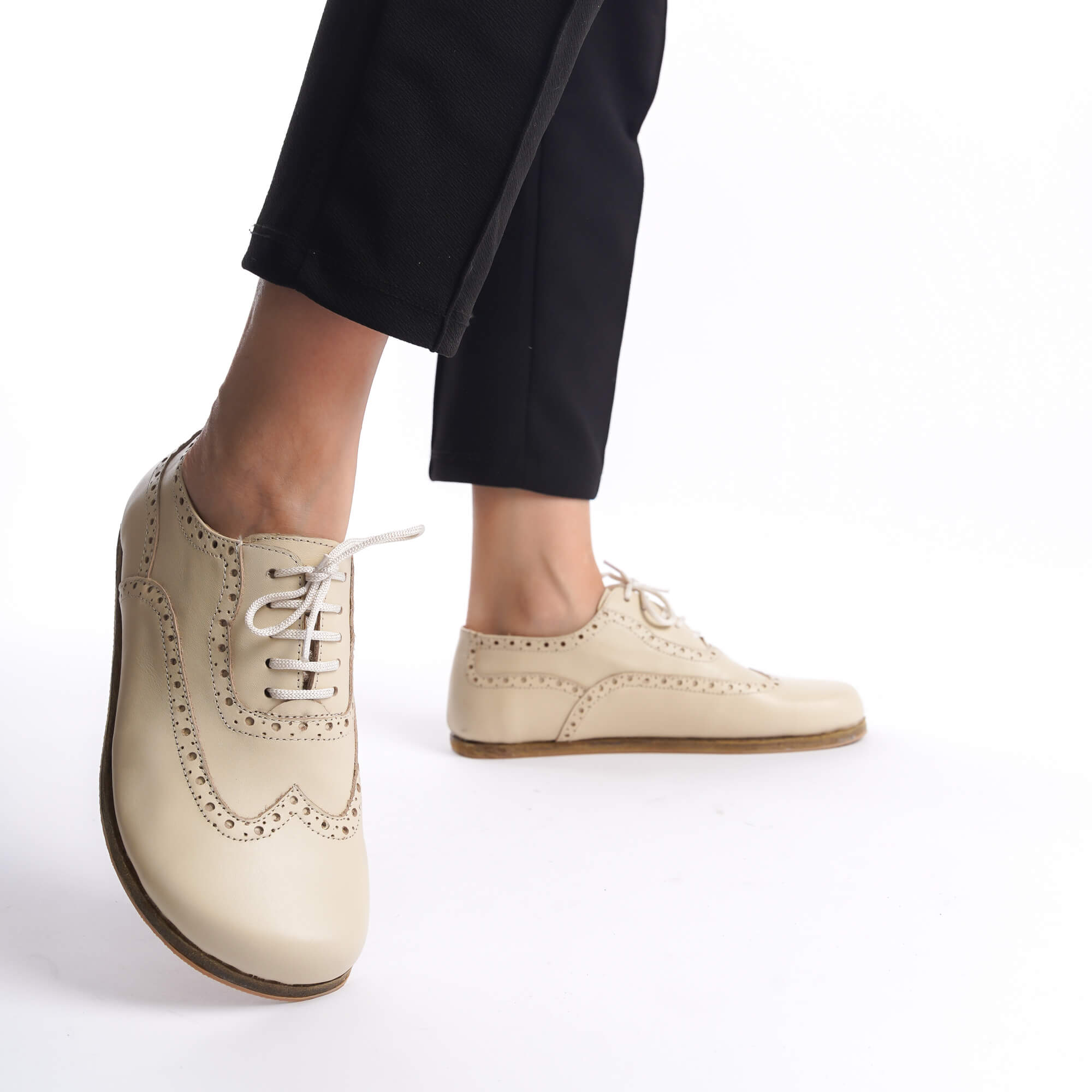 Close-up of a woman's feet in beige Doris leather barefoot women's oxfords, showcasing their elegant design against a white background.