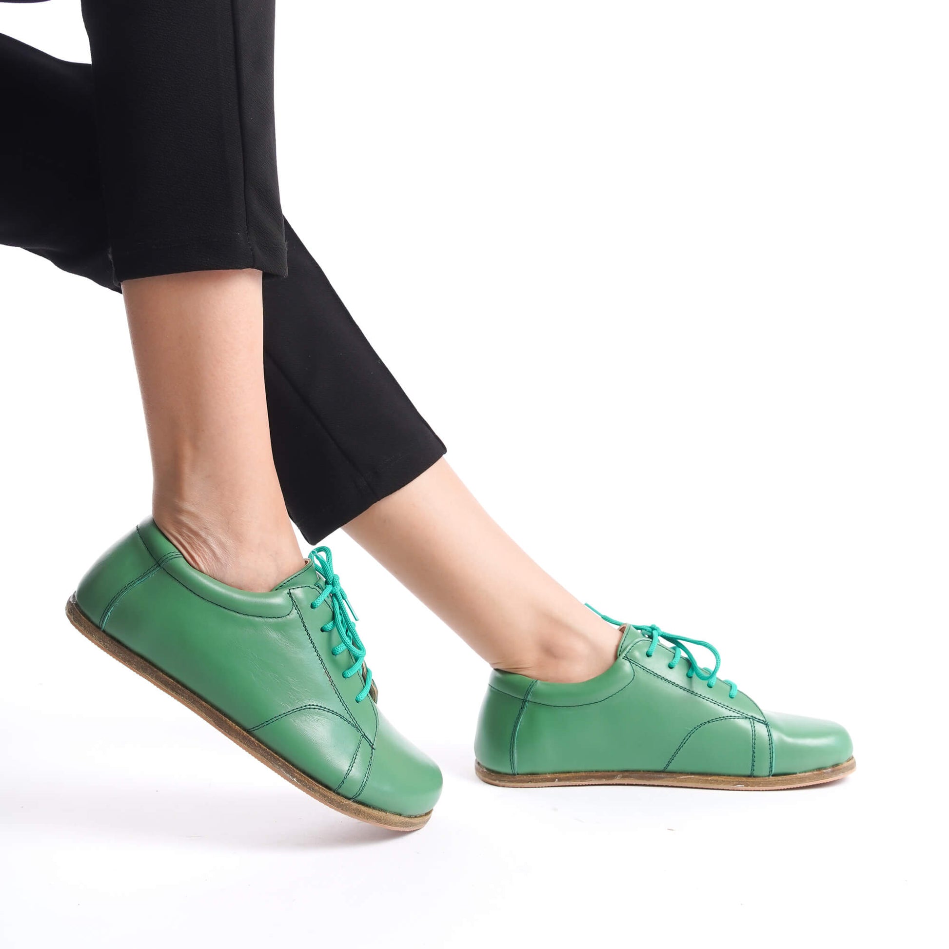 Close-up of Lydia Leather Barefoot Women Sneakers in green with turquoise laces, highlighting their elegant design and comfortable fit.