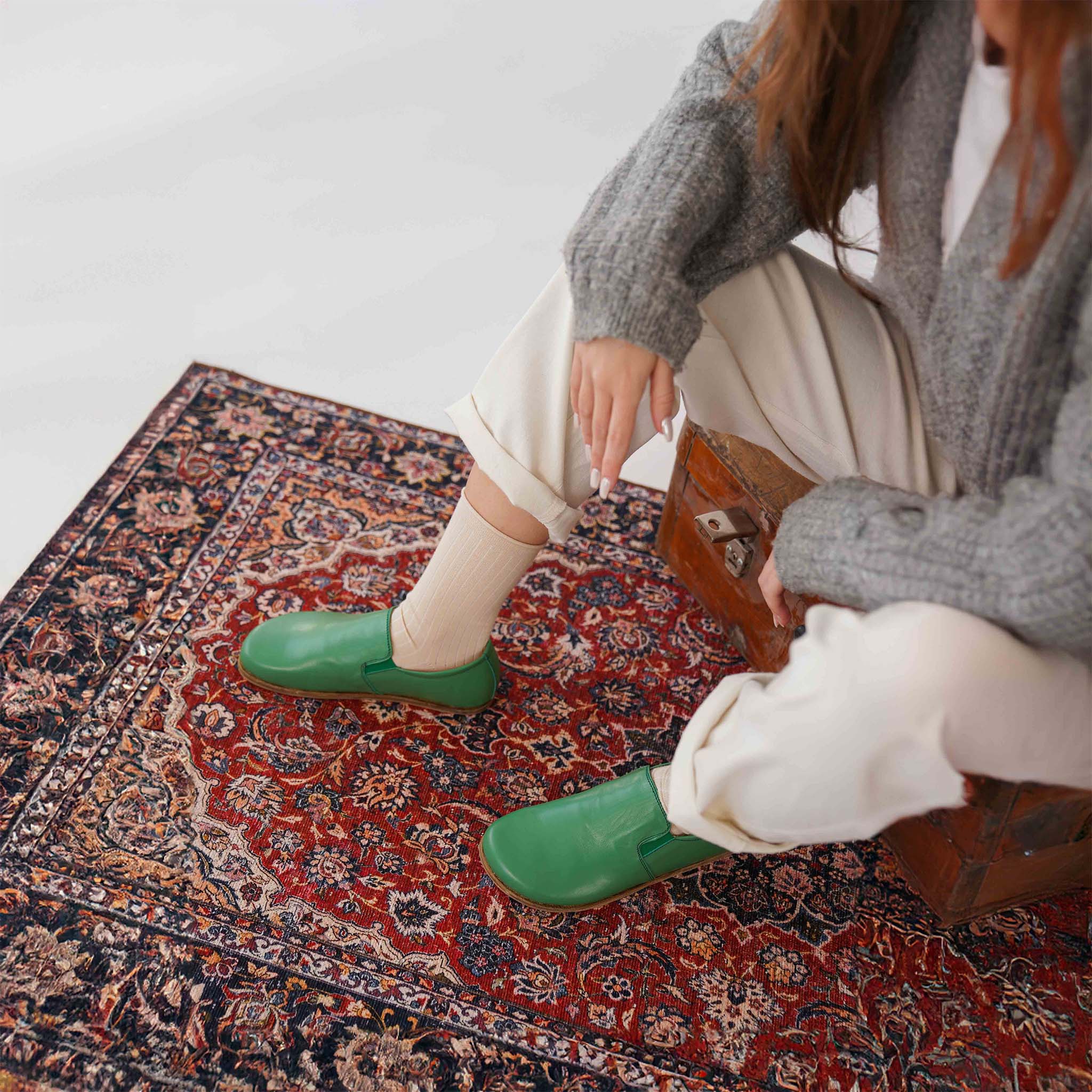 Model showcasing green leather loafers on a patterned rug. Pelanir's minimalist shoes for women.