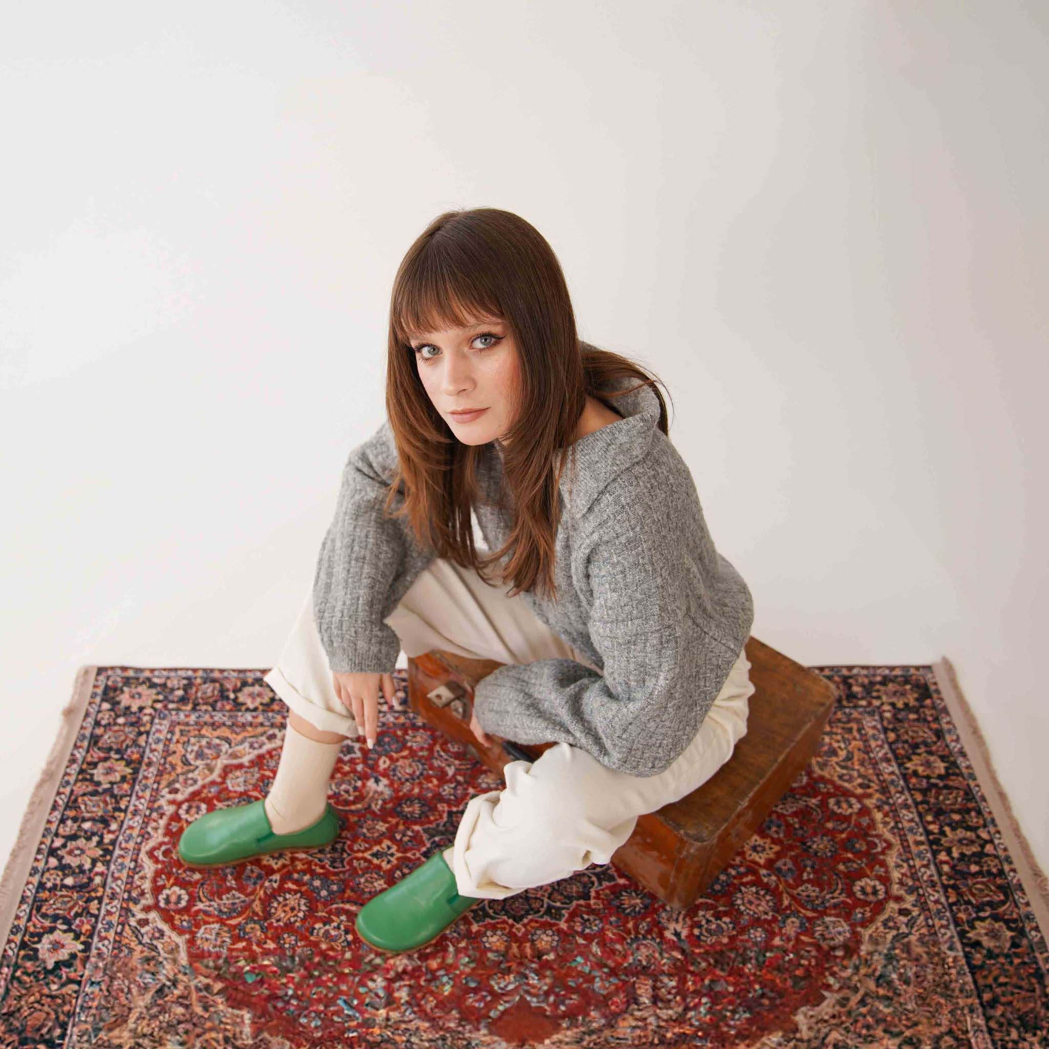 Stylish green leather loafers on model, sitting on a vintage suitcase. Discover minimalist footwear at Pelanir.