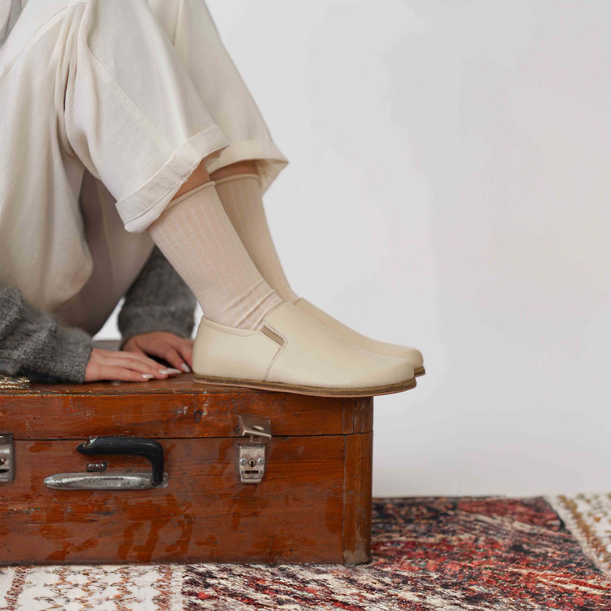 Model seated, showing Ionia beige loafers with white pants - Embrace simplicity with Ionia Leather Barefoot Women Loafers in beige.