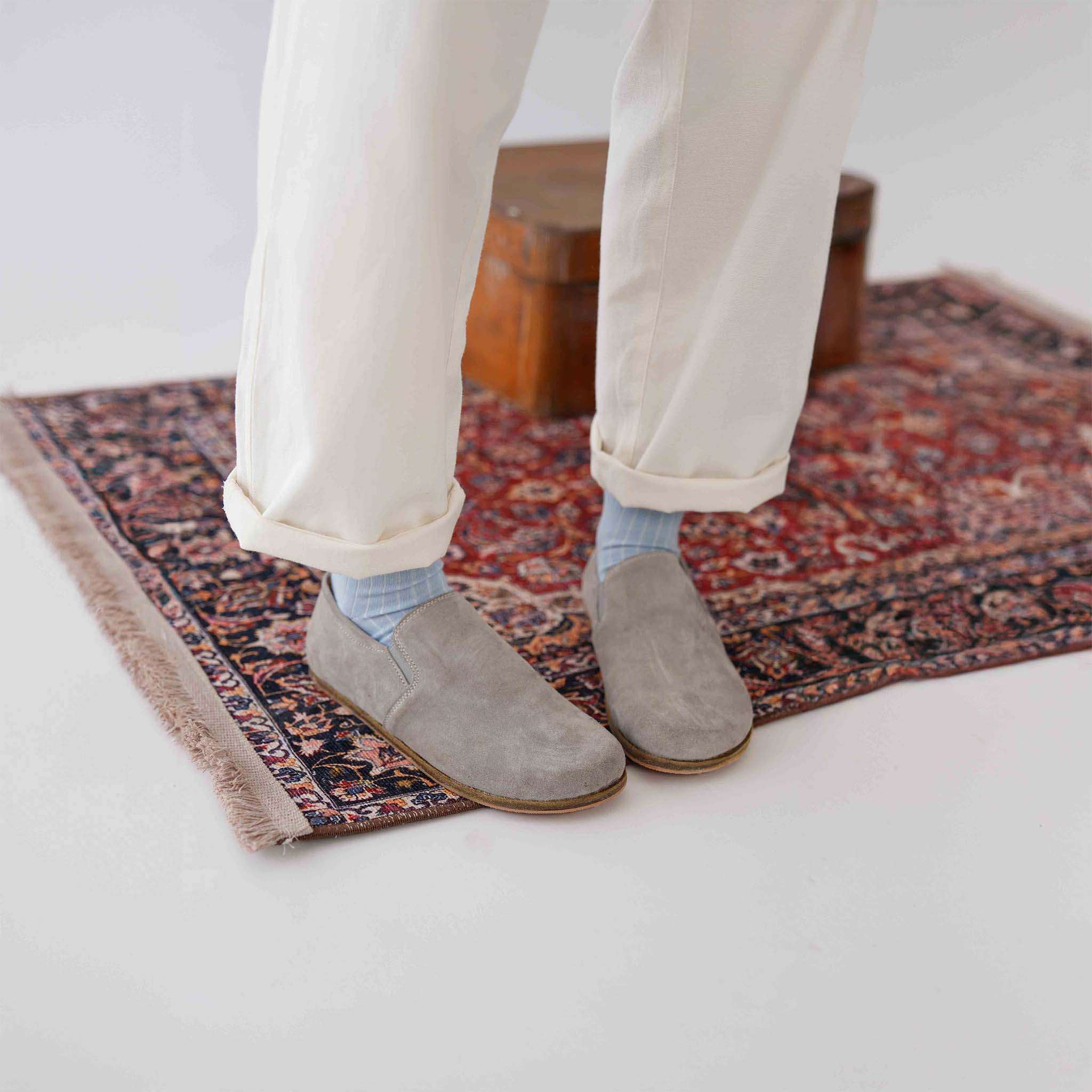 Gray suede loafers with light blue socks, resting on a vintage suitcase, showcasing their versatile style.