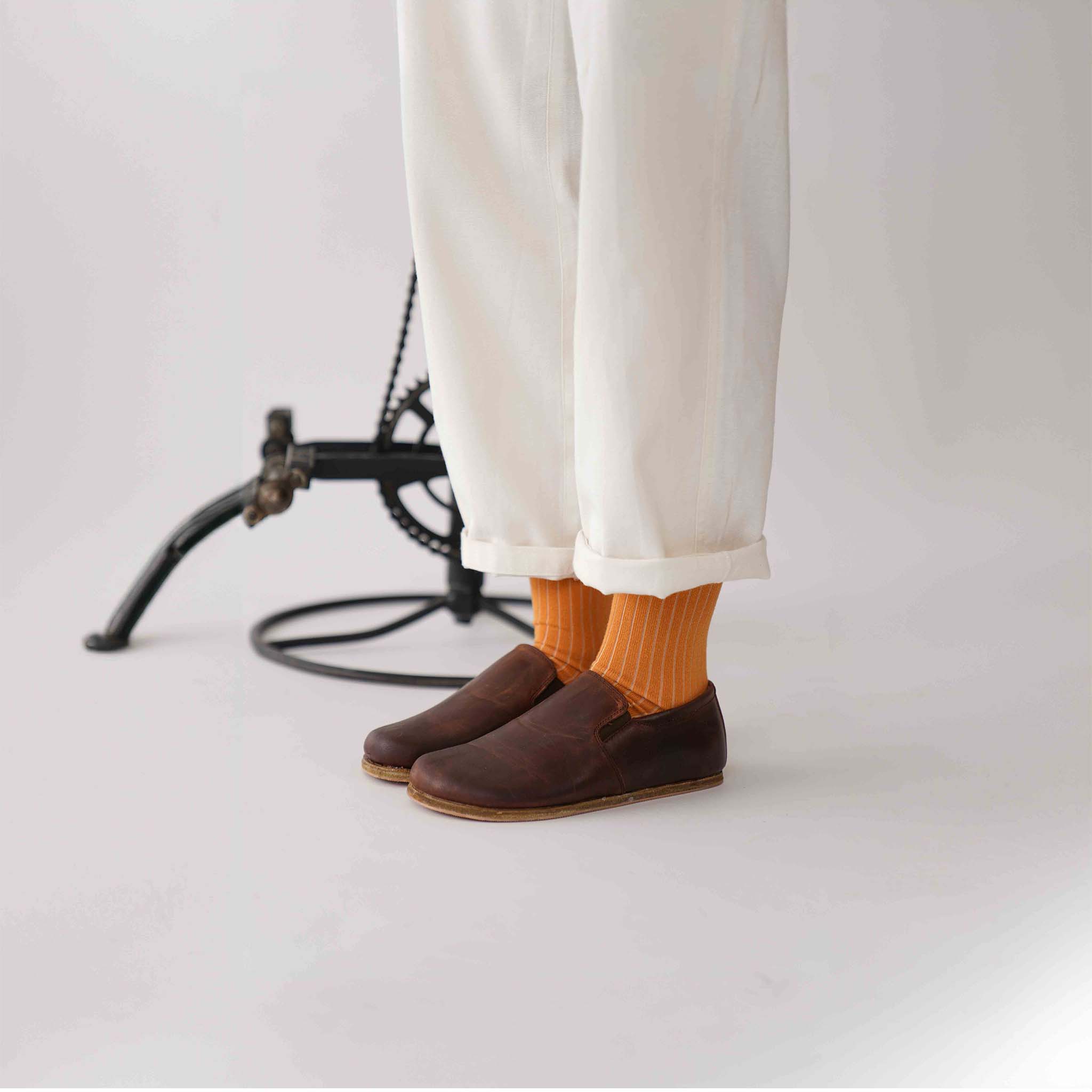 Side view of Ionia Leather Barefoot Women Loafers in brown, paired with white pants and orange socks.