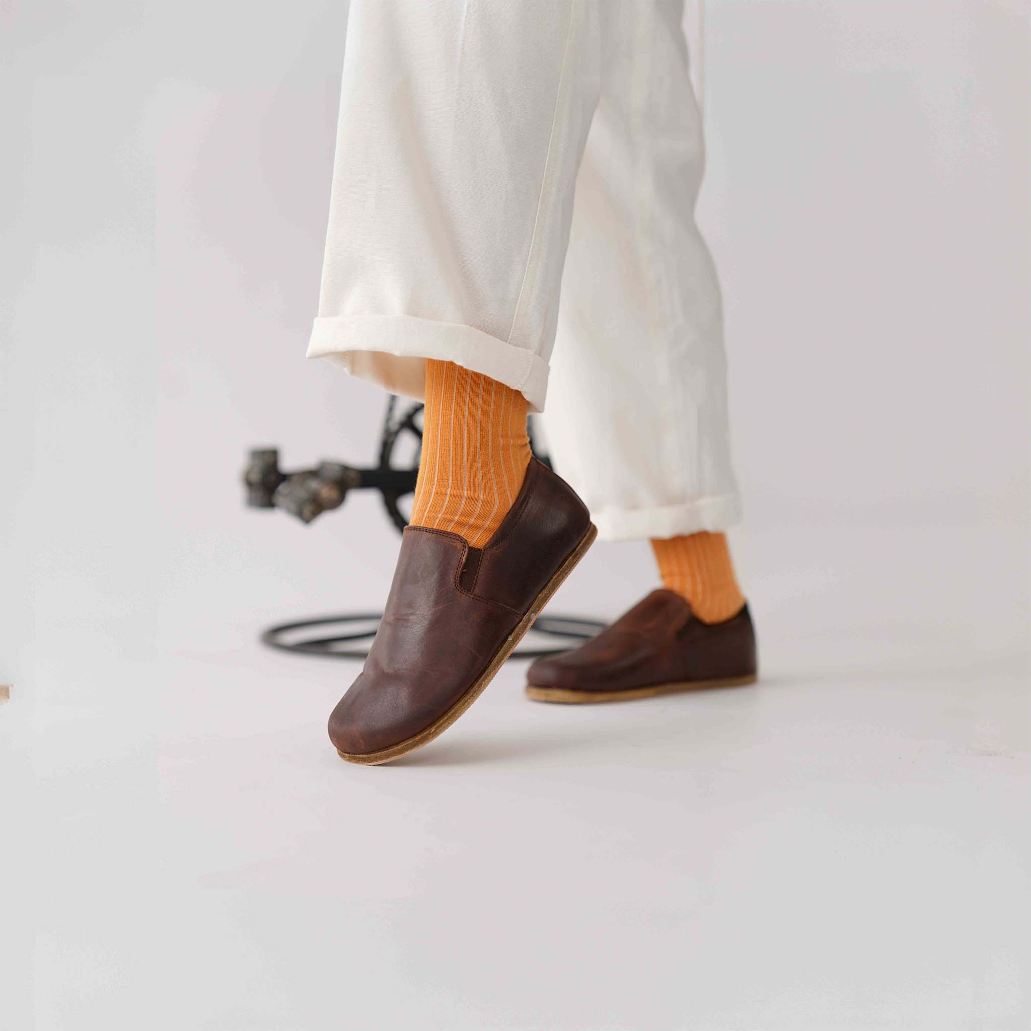 View of Ionia Leather Barefoot Women Loafers in brown, paired with white pants and orange socks.