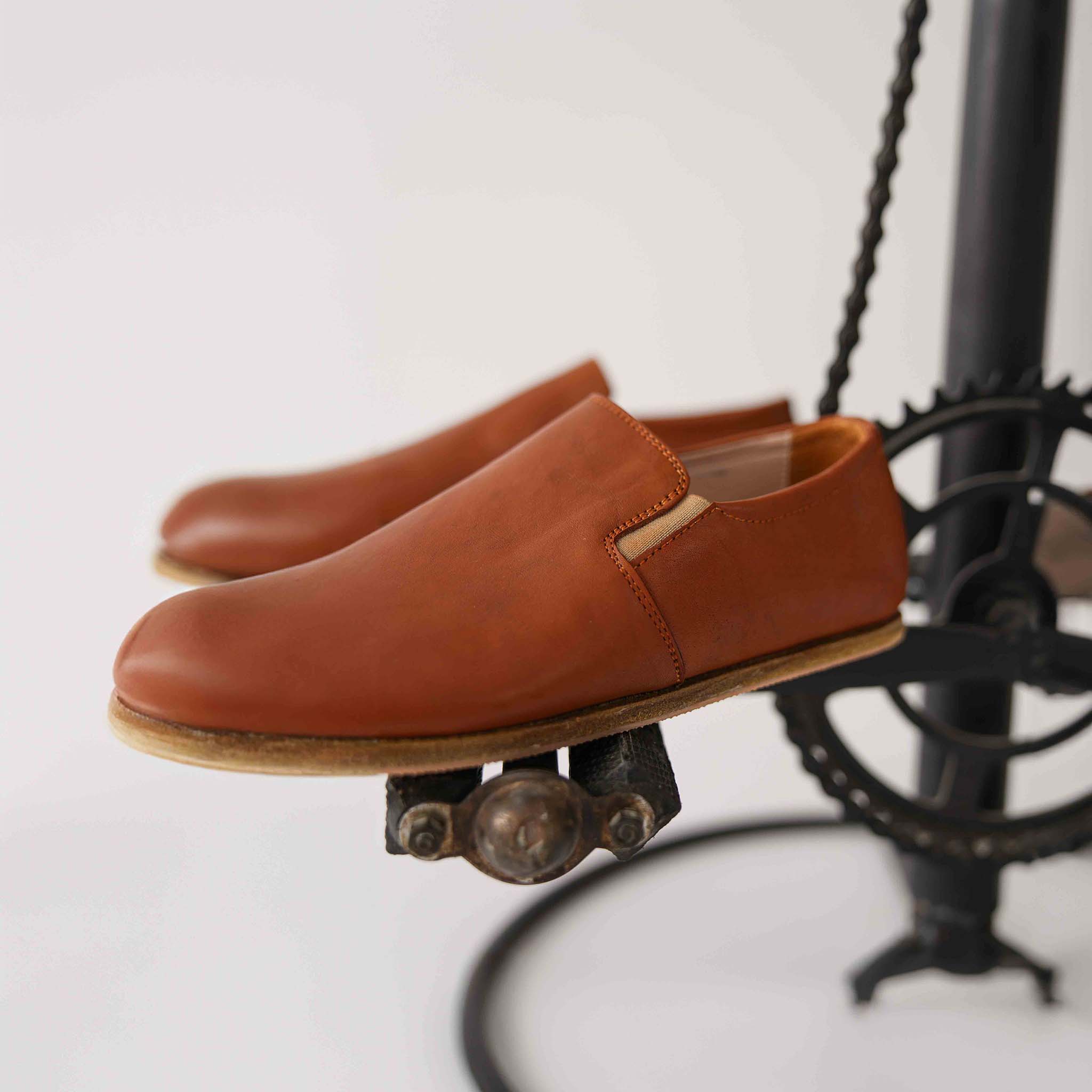 Tan brown Ionia Leather Barefoot Women Loafers displayed on a vintage metal stand, showcasing the fine craftsmanship and high-quality leather.