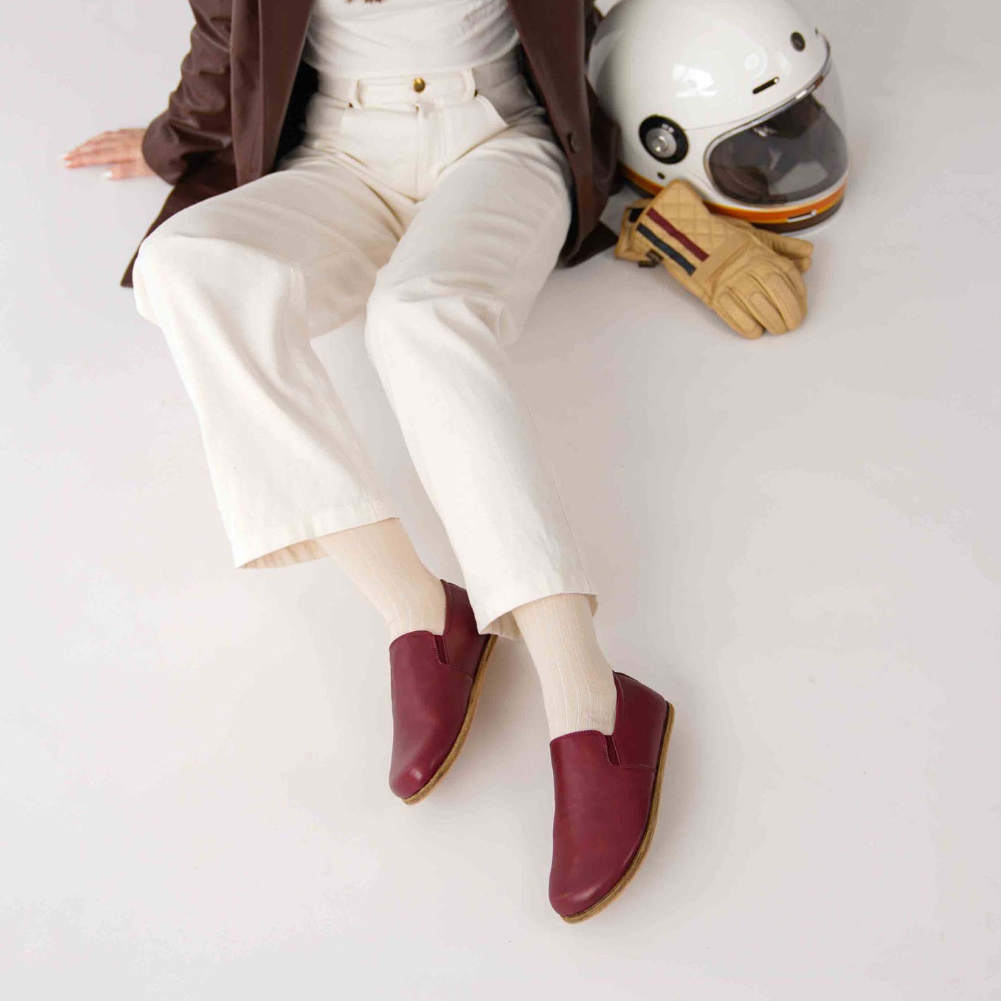 Model seated with Burgundy loafers, a leather jacket, and accessories.