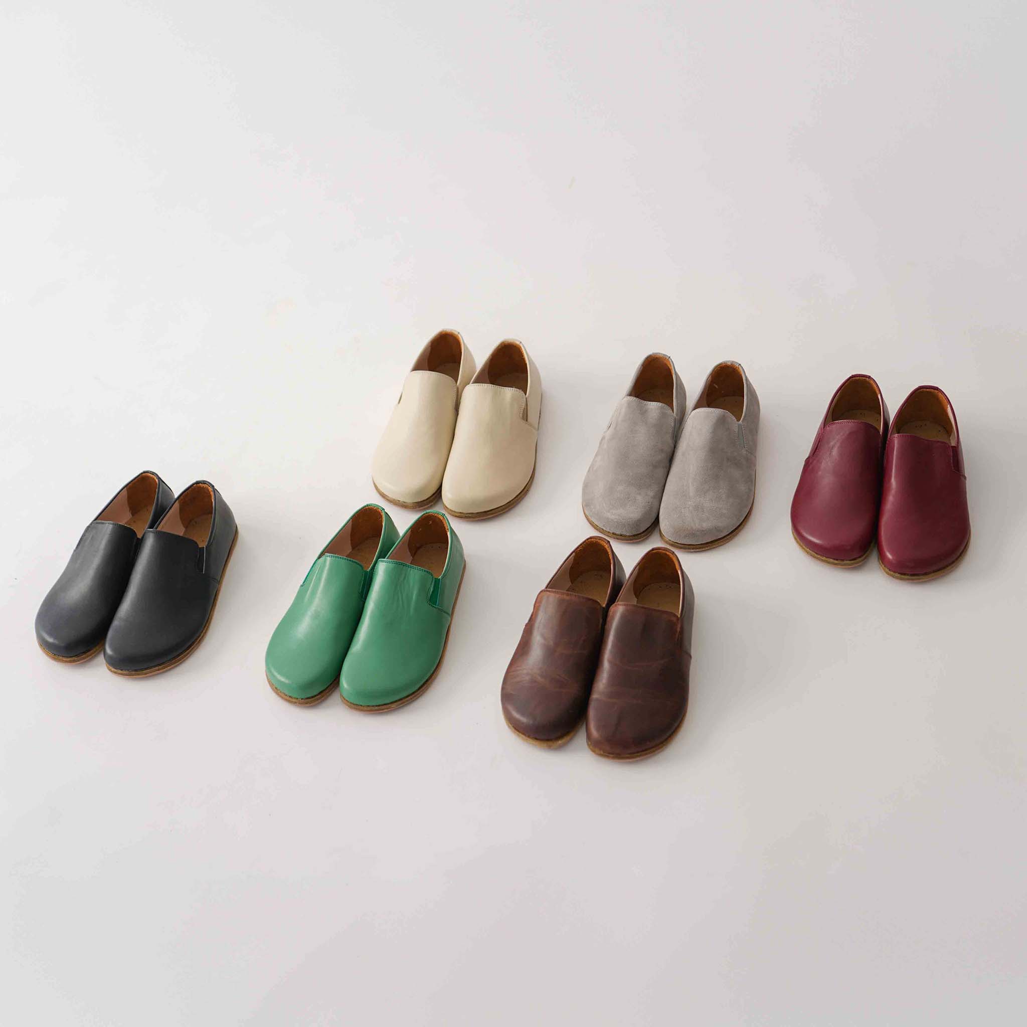 Collection of barefoot loafers in various colors including brown, displayed in a minimalist setting.