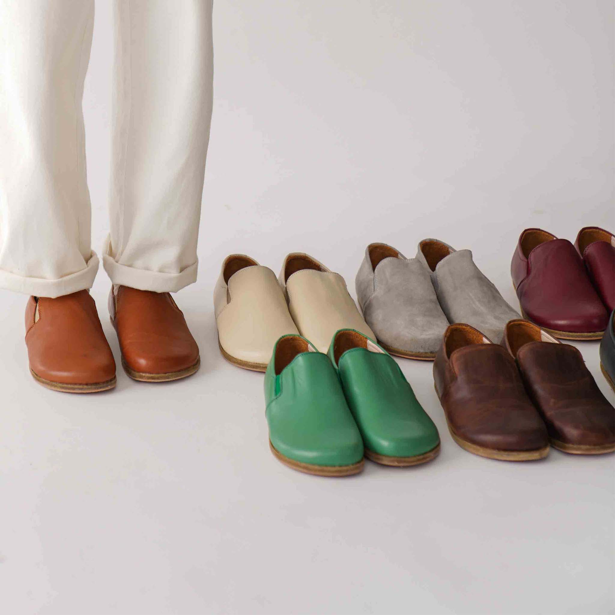 Model wearing tan brown Ionia Leather Barefoot Women Loafers, standing next to a variety of colored loafers, highlighting the versatile color options.