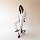Model sitting on a modern stool, wearing white outfit and Aeolia Brown Loafers, showcasing the stylish and comfortable fit.
