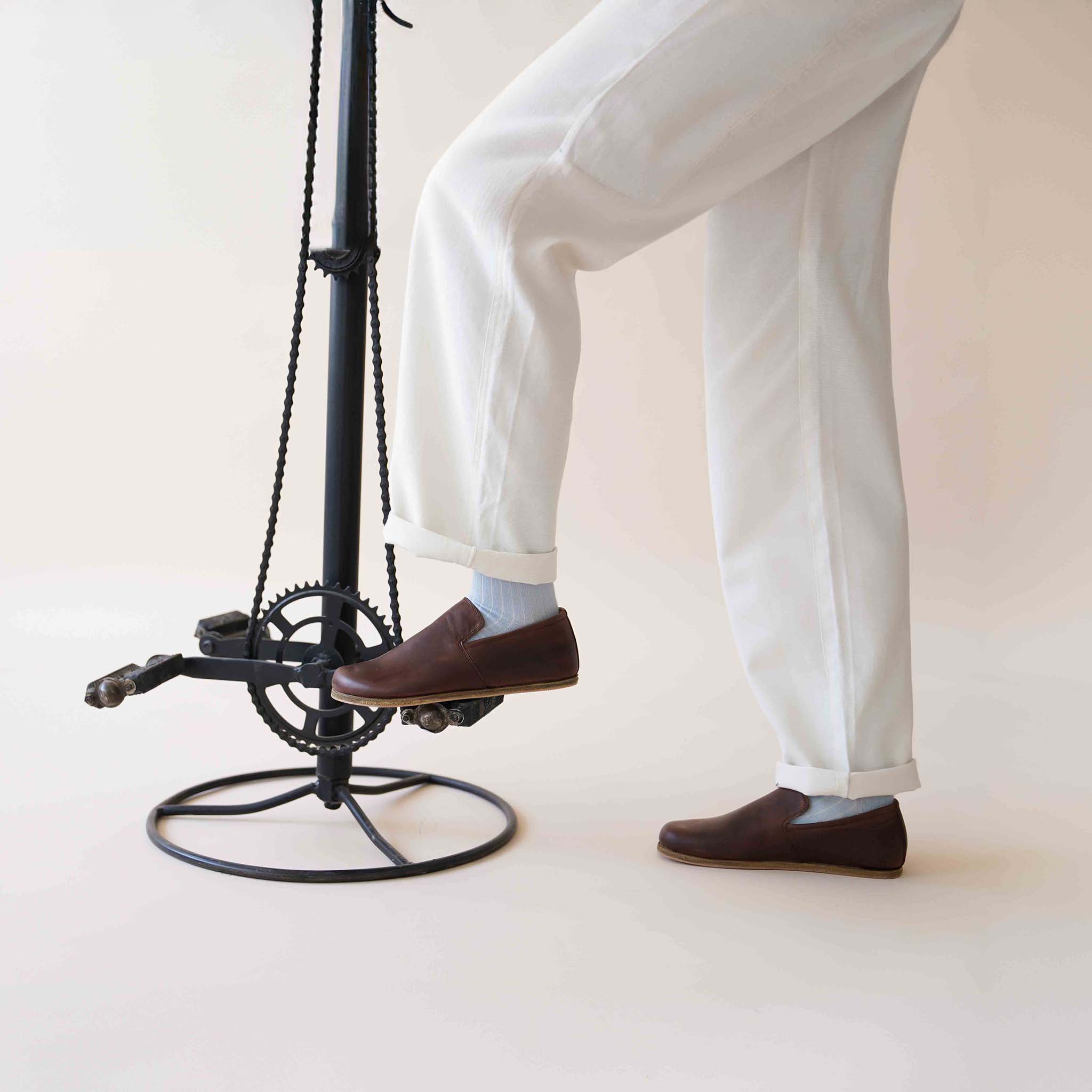 Model wearing Aeolia Brown Loafers with white pants, foot resting on a modern stool, showcasing the shoe's elegant design and comfortable fit.