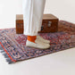 Model wearing Aeolia Beige Women Loafers with orange socks, standing on a patterned rug, next to a suitcase, highlighting the stylish fit.