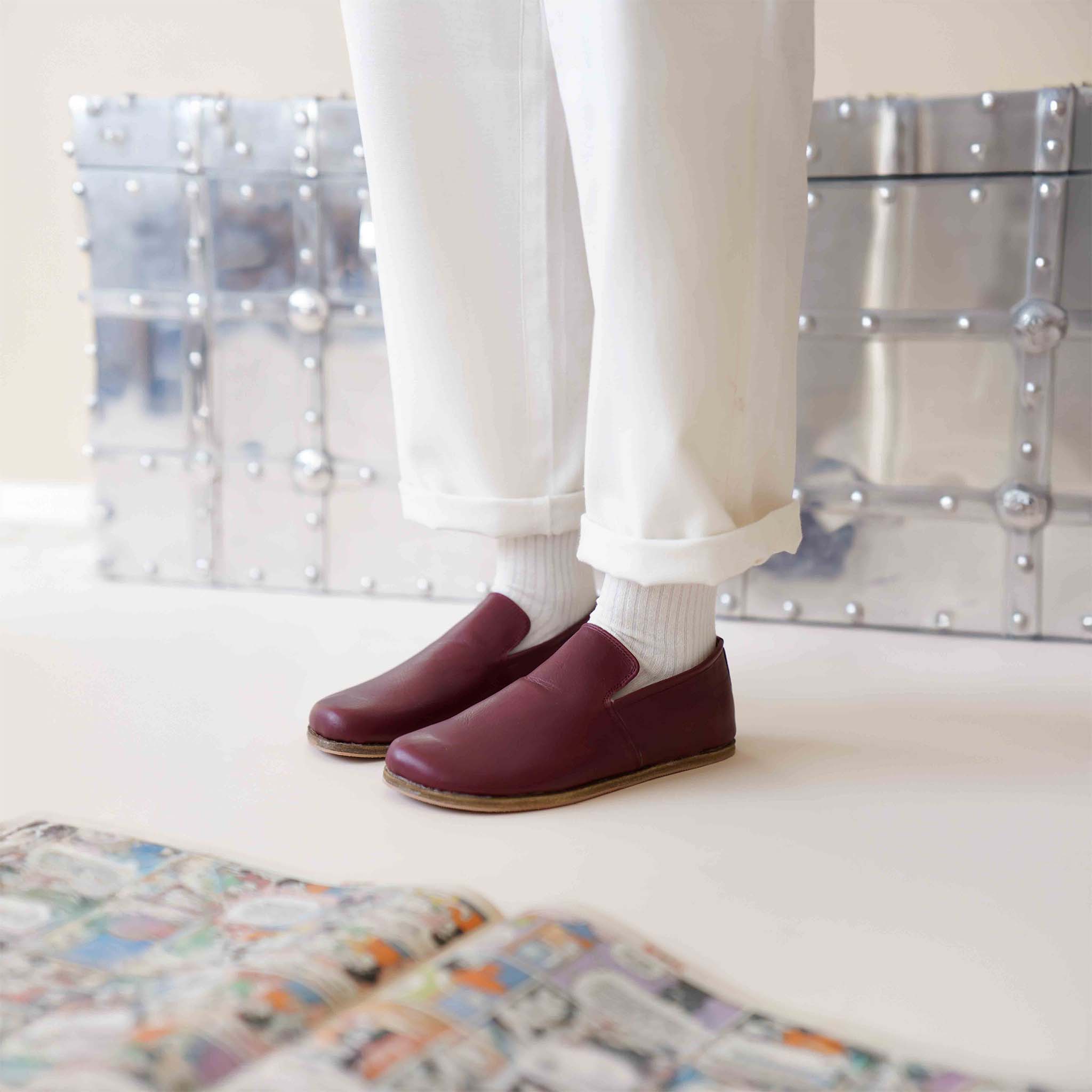 Aeolia Leather Barefoot Women Loafers in Burgundy, paired with white pants and socks, with a comic book and metal chest.