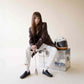 Model Sitting on a Metallic Chest, Wearing Aeolia Leather Barefoot Women Loafers in Black with a Stylish Outfit.