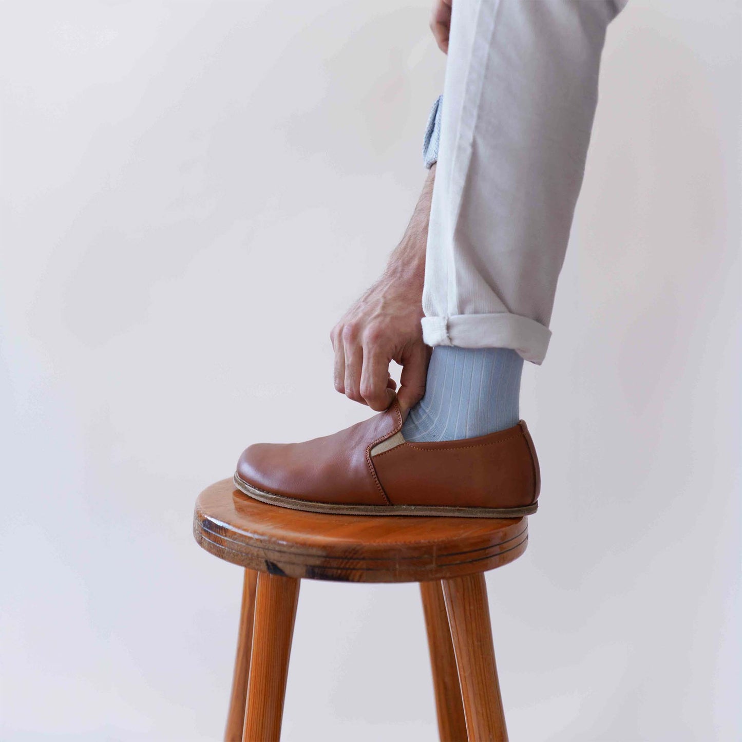 Man adjusting his tan brown Ionia leather loafers while sitting on a wooden stool, featuring genuine leather and natural fit, available at pelanir.com.