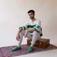 Man wearing green Ionia leather barefoot loafers, sitting on a vintage trunk. Discover more at pelanir.com!