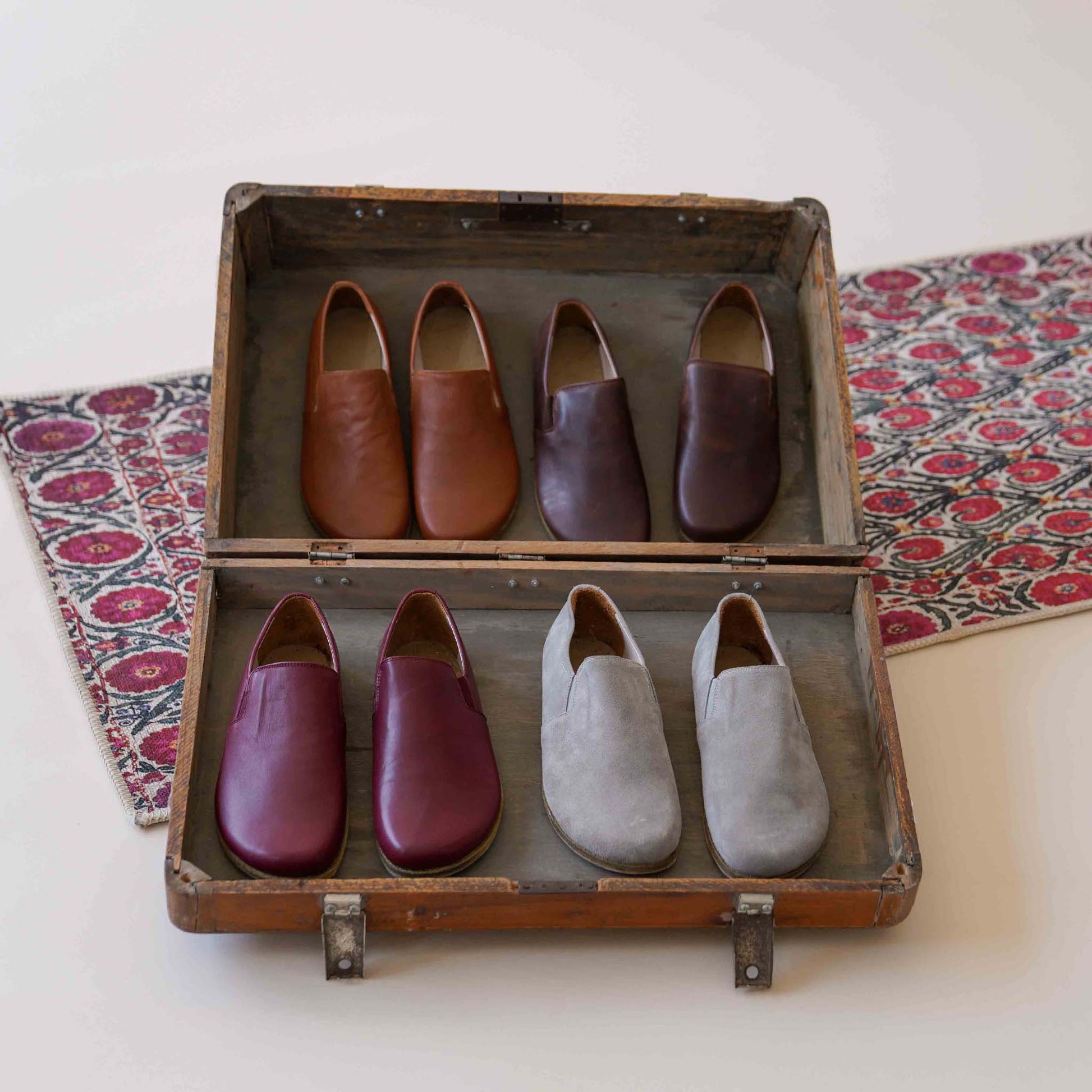 Vintage suitcase displaying Ionia Leather Barefoot Men Loafers in various colors, including burgundy, brown, and gray, emphasizing variety and style.