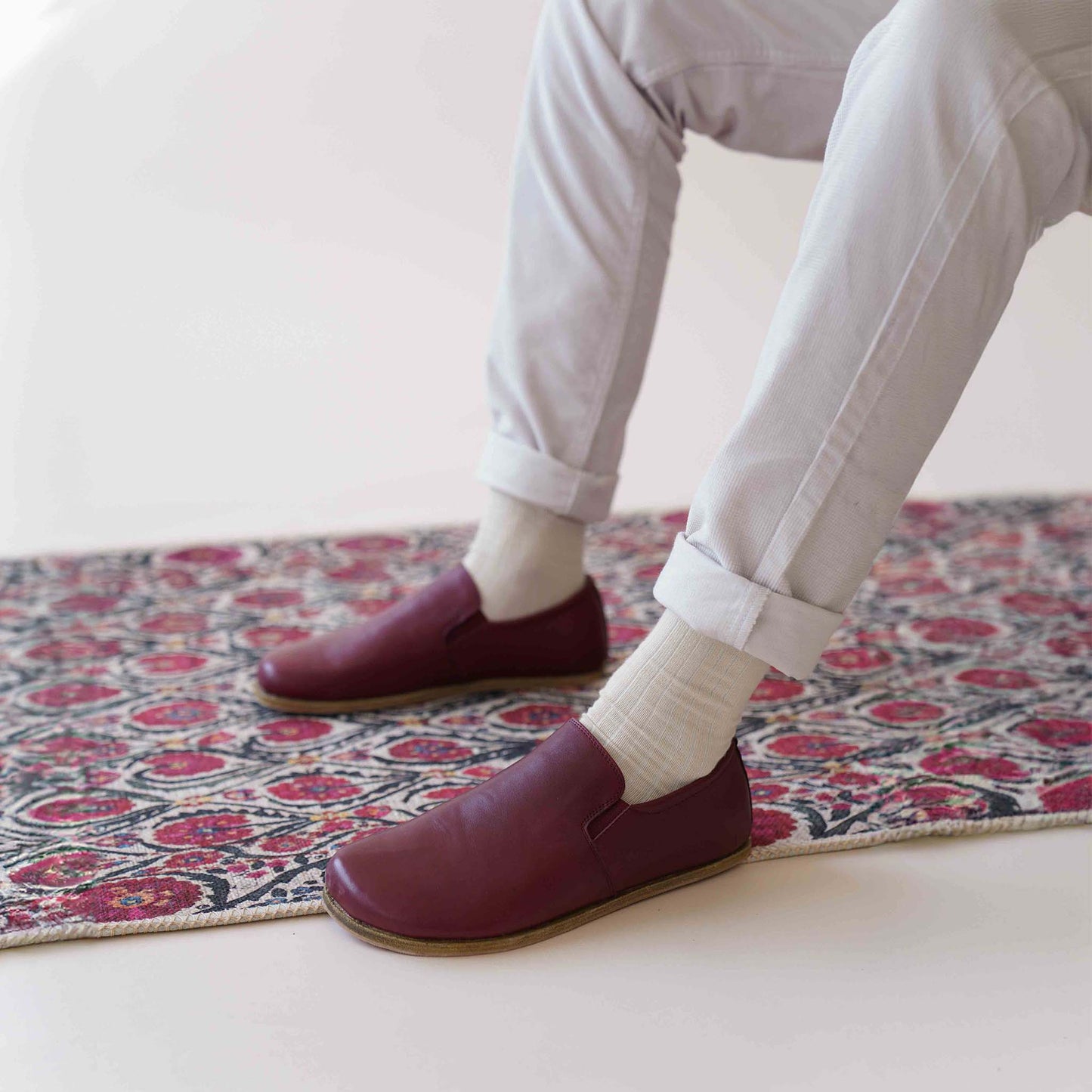 Close-up of a man sitting on a rug wearing Ionia Leather Barefoot Men Loafers in Burgundy, showcasing their flexibility and comfort.