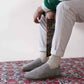 Man sitting on a rug with legs crossed, holding a book, wearing Gray Suede Ionia Leather Barefoot Men's Loafers.