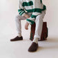 Man sitting with a backpack, wearing brown Ionia Leather Barefoot Men Loafers paired with white socks and light pants.