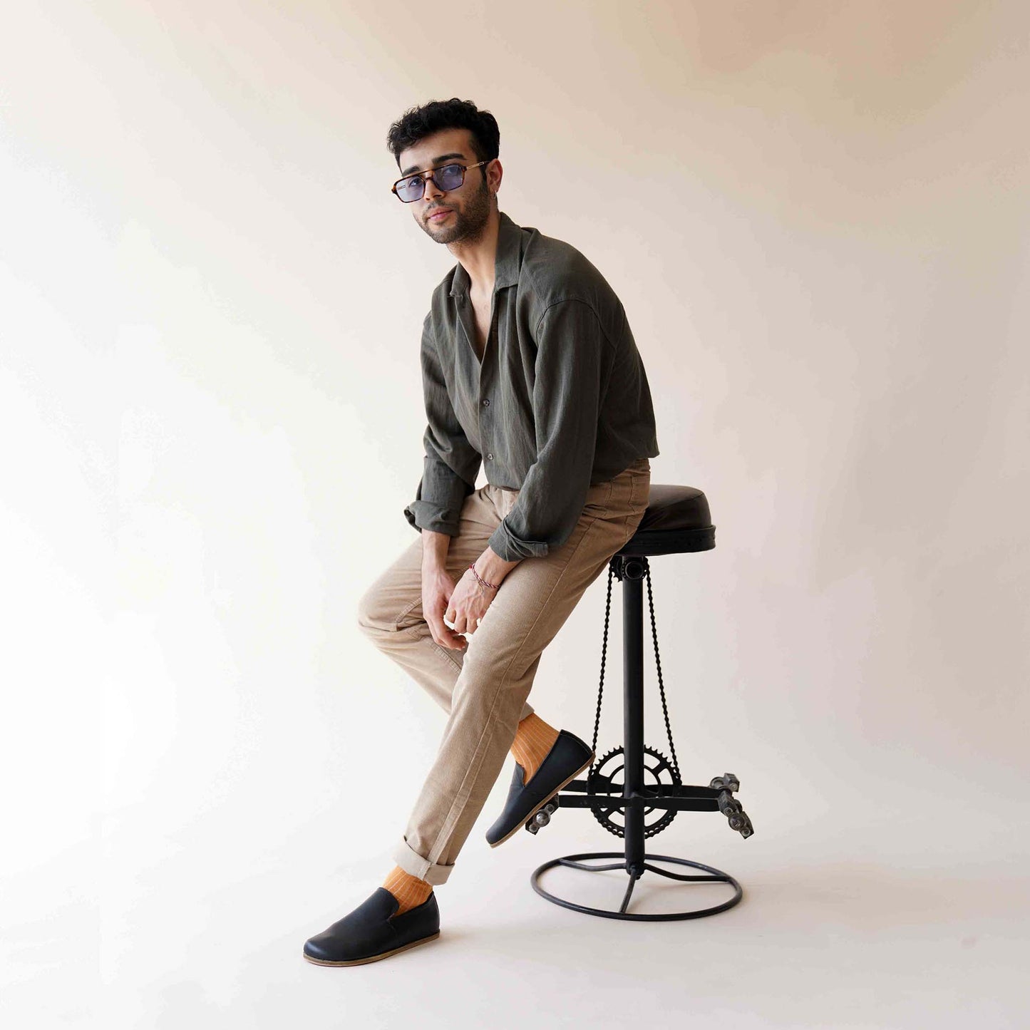 Model wearing Aeolia Leather Barefoot Men's Loafers in black, sitting on a stool in stylish casual attire. Shop at pelanir.com!