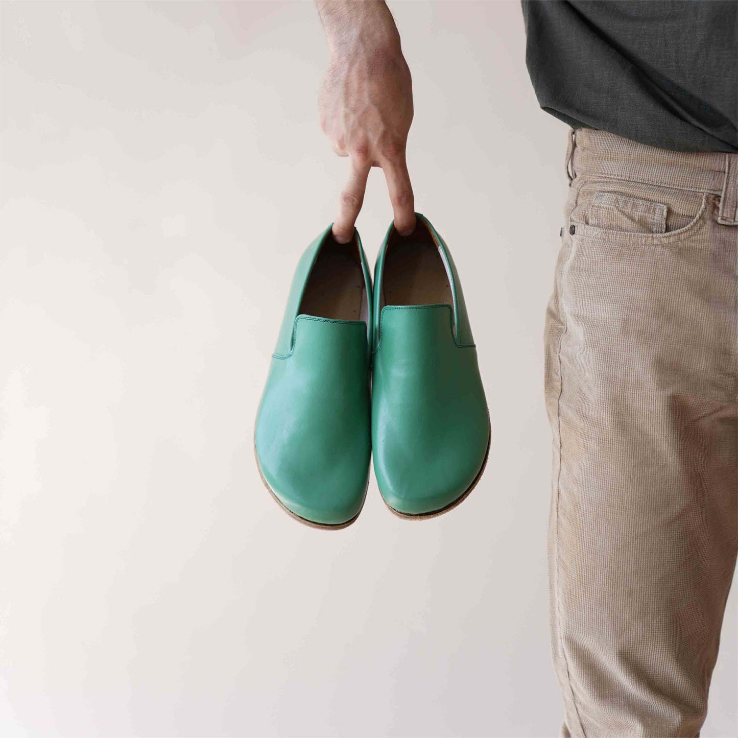 Hand holding a pair of Green Aeolia Leather Barefoot Men's Loafers, showcasing the sleek and stylish design.