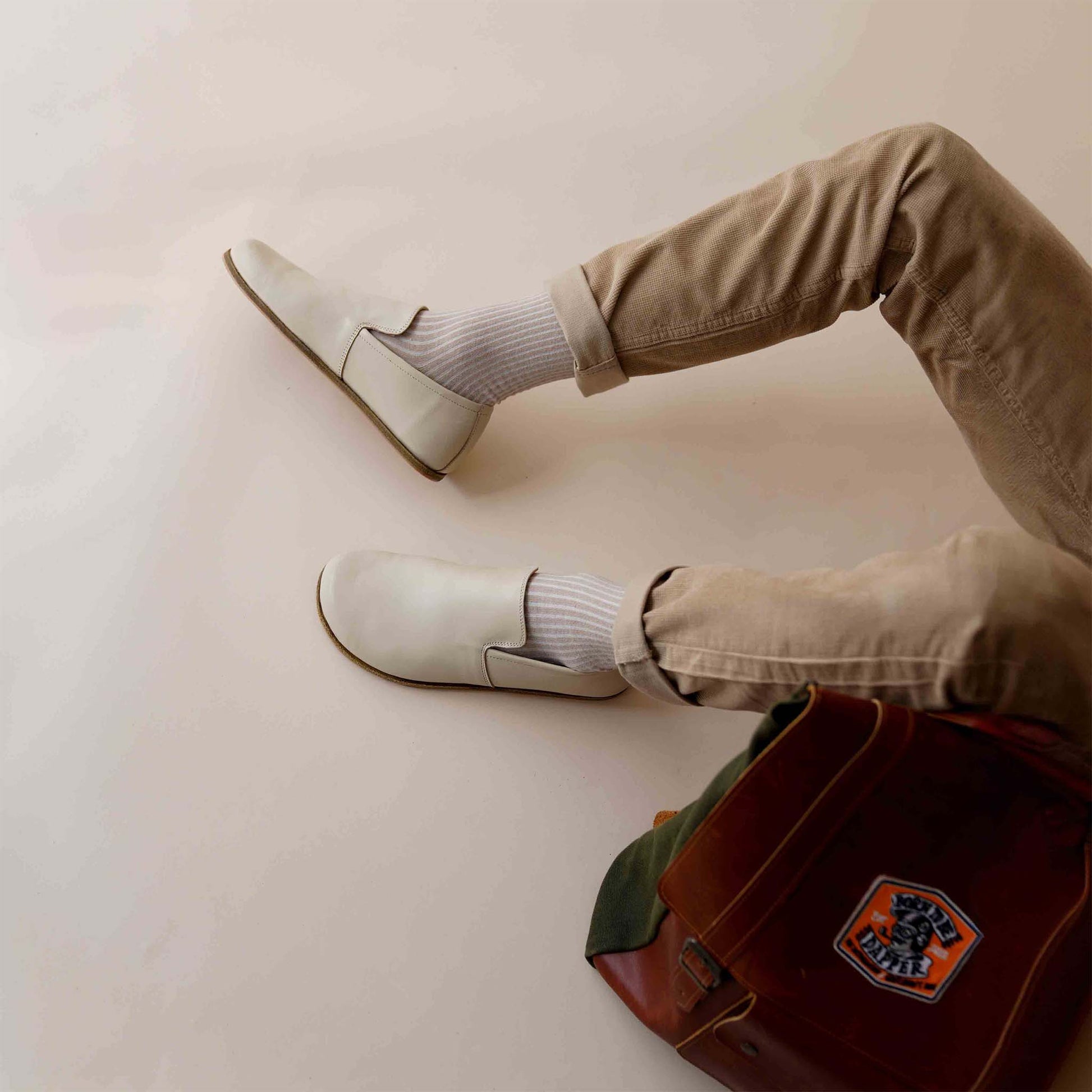 Man lounging in beige Aeolia Leather Barefoot Men's Loafers, beige pants, and white socks. Shop at pelanir.com!