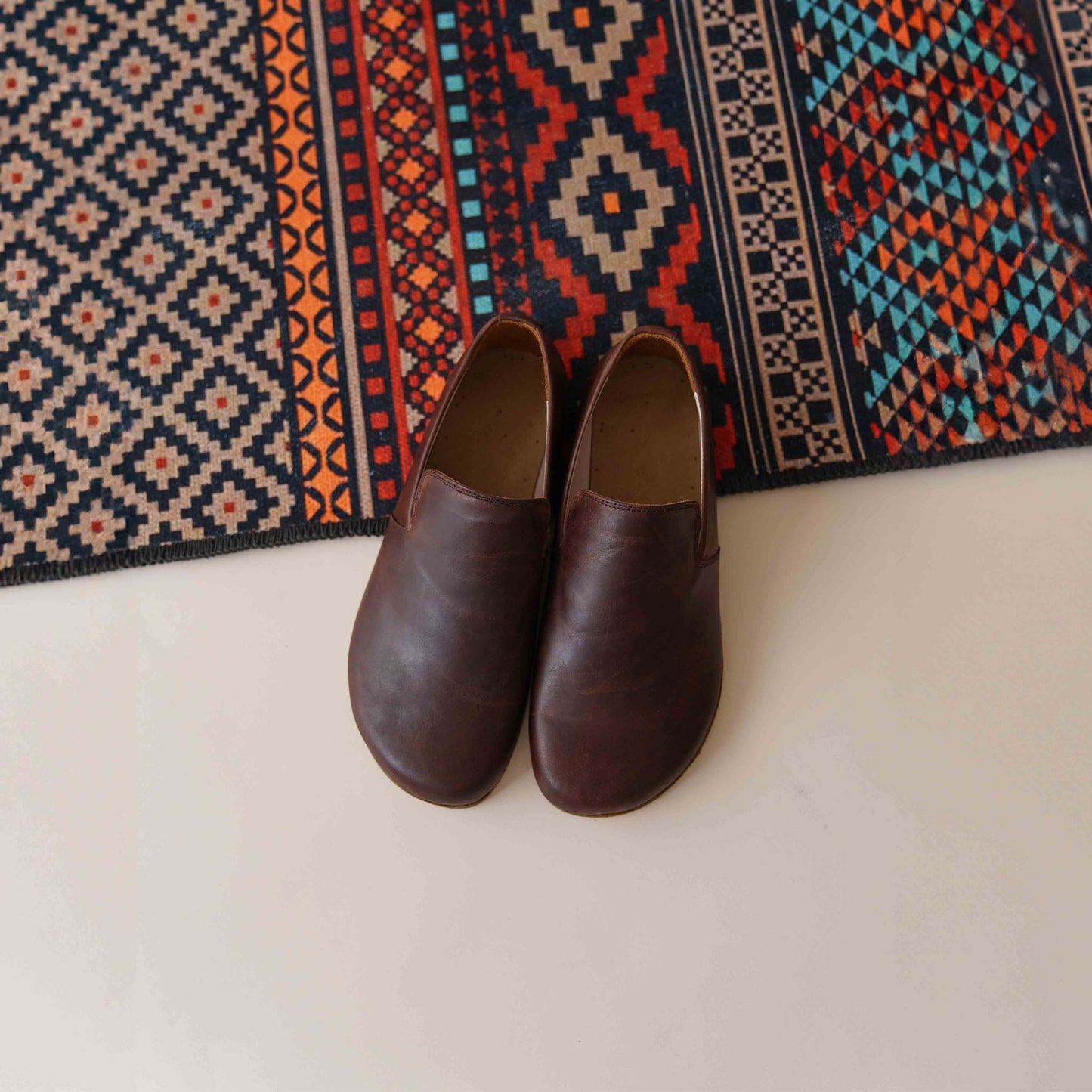 Pair of Aeolia brown leather barefoot men loafers displayed on a colorful rug, ideal for promoting natural walking. Shop now at pelanir.com!