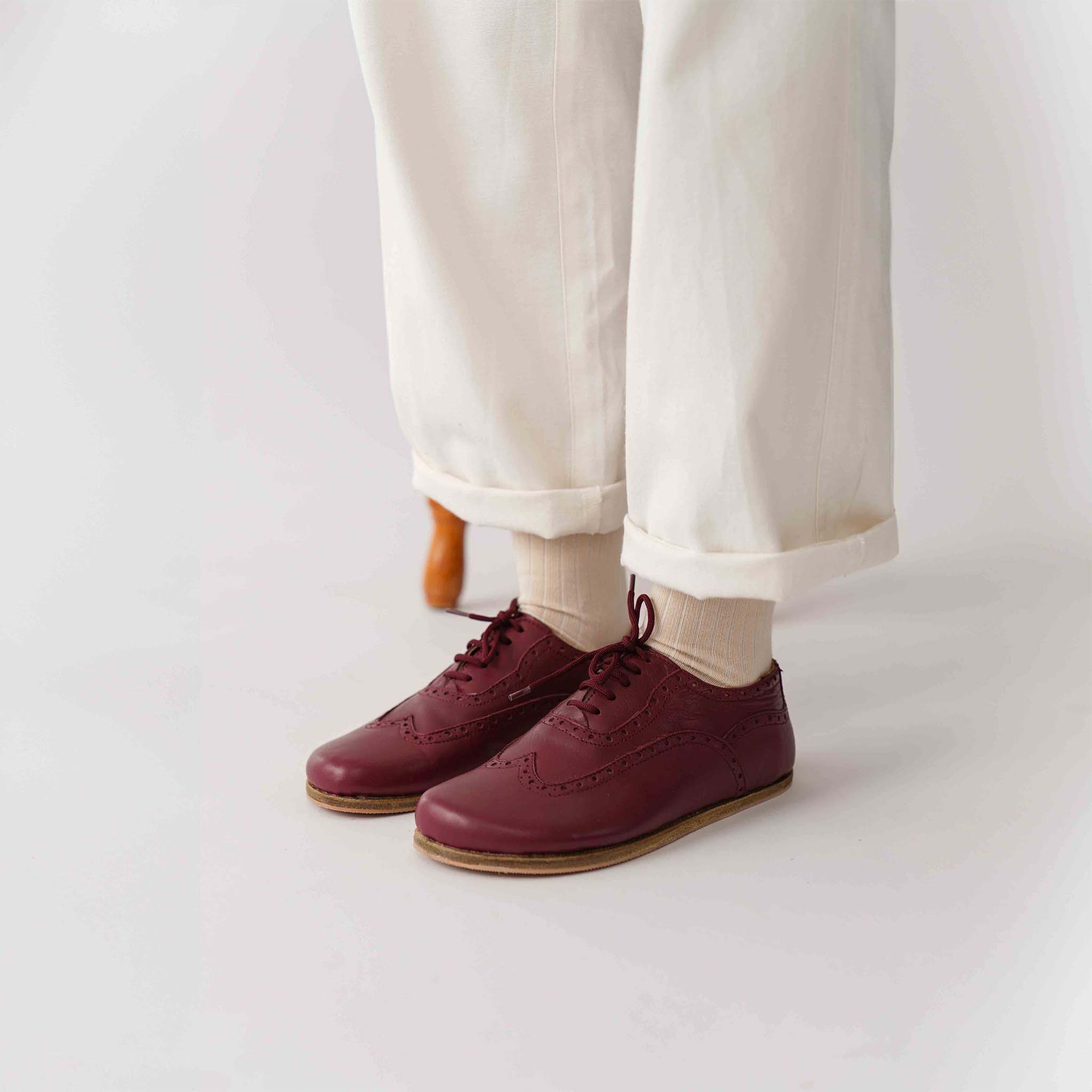 Close-up side view of Doris leather barefoot women Oxfords in Burgundy, worn by a person in black pants.