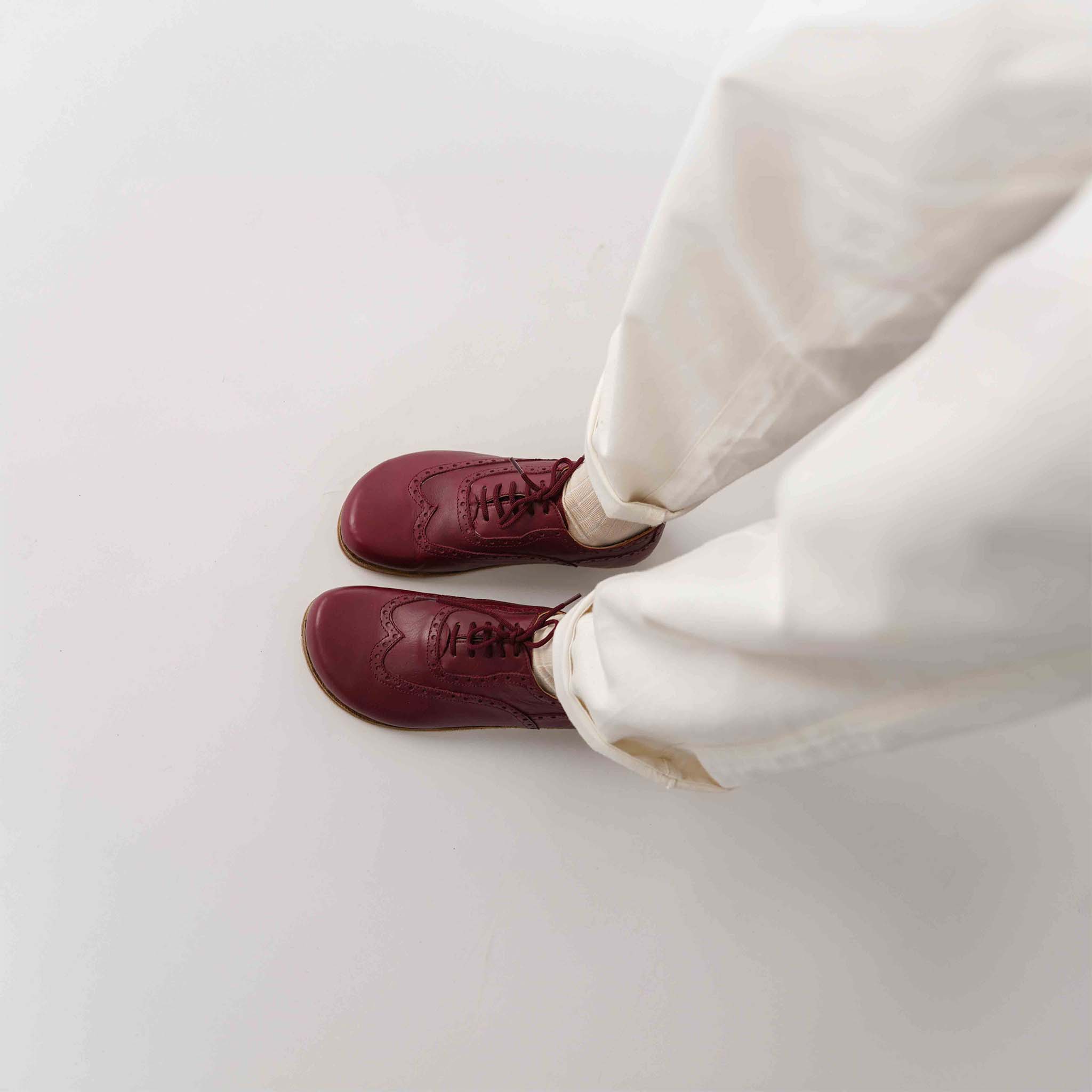 Overhead view of a person wearing Doris leather barefoot women Oxfords in Burgundy with white pants.